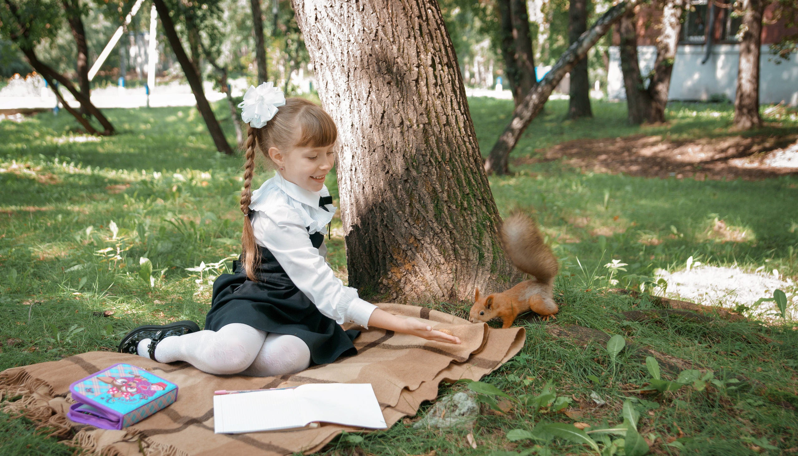 Детская фотосессия осенью - школьница сидя у дерева подзывает белку