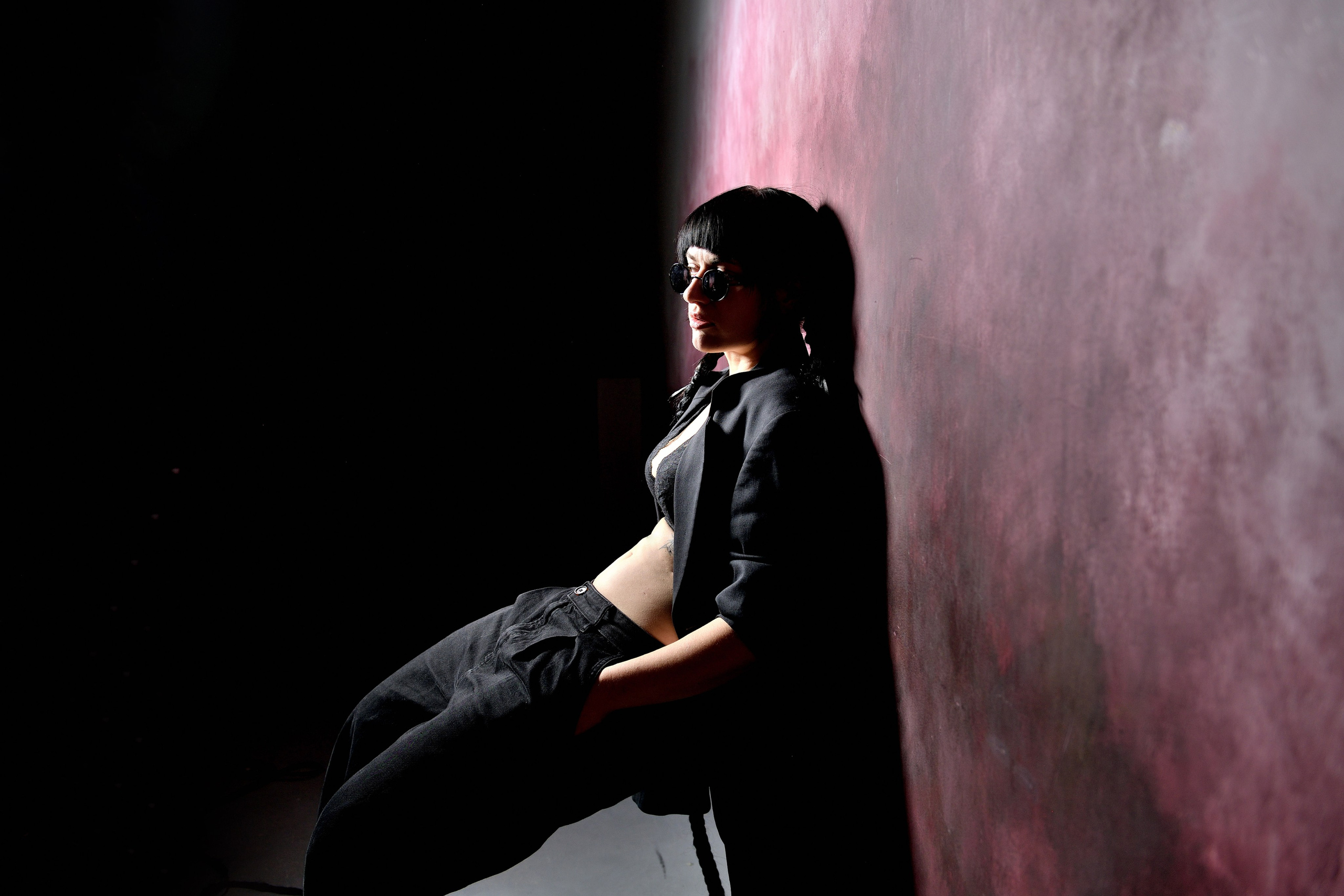 Девушка в полутонах и темном свете позирует на фоне цветной стены.