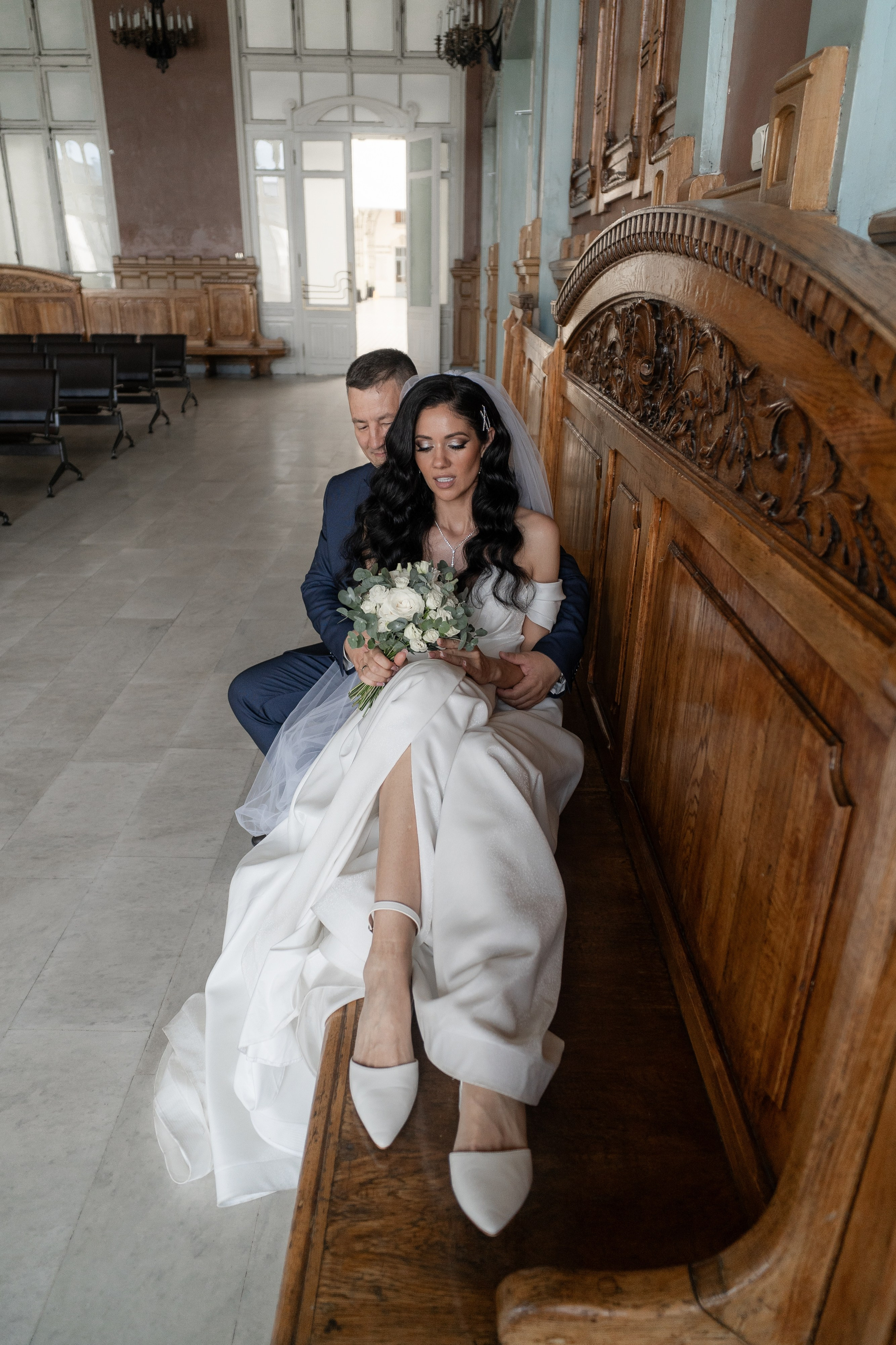 Свадебная фотография на Витебском вокзале в Санкт-Петербурге Жених и невеста обнимаются на коричневой скамейке