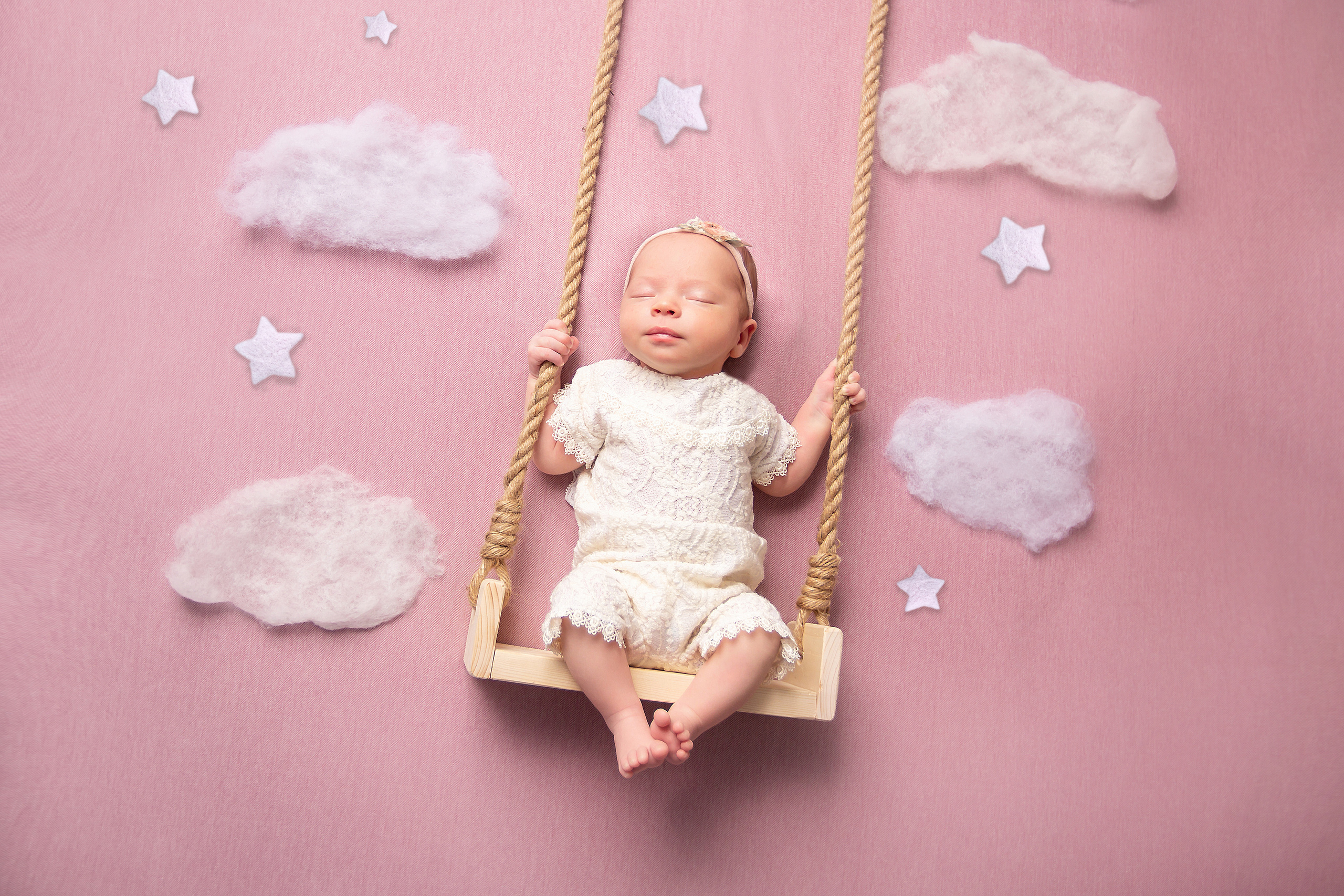 новорожденный малыш на качелях с нежно-розовым фоном