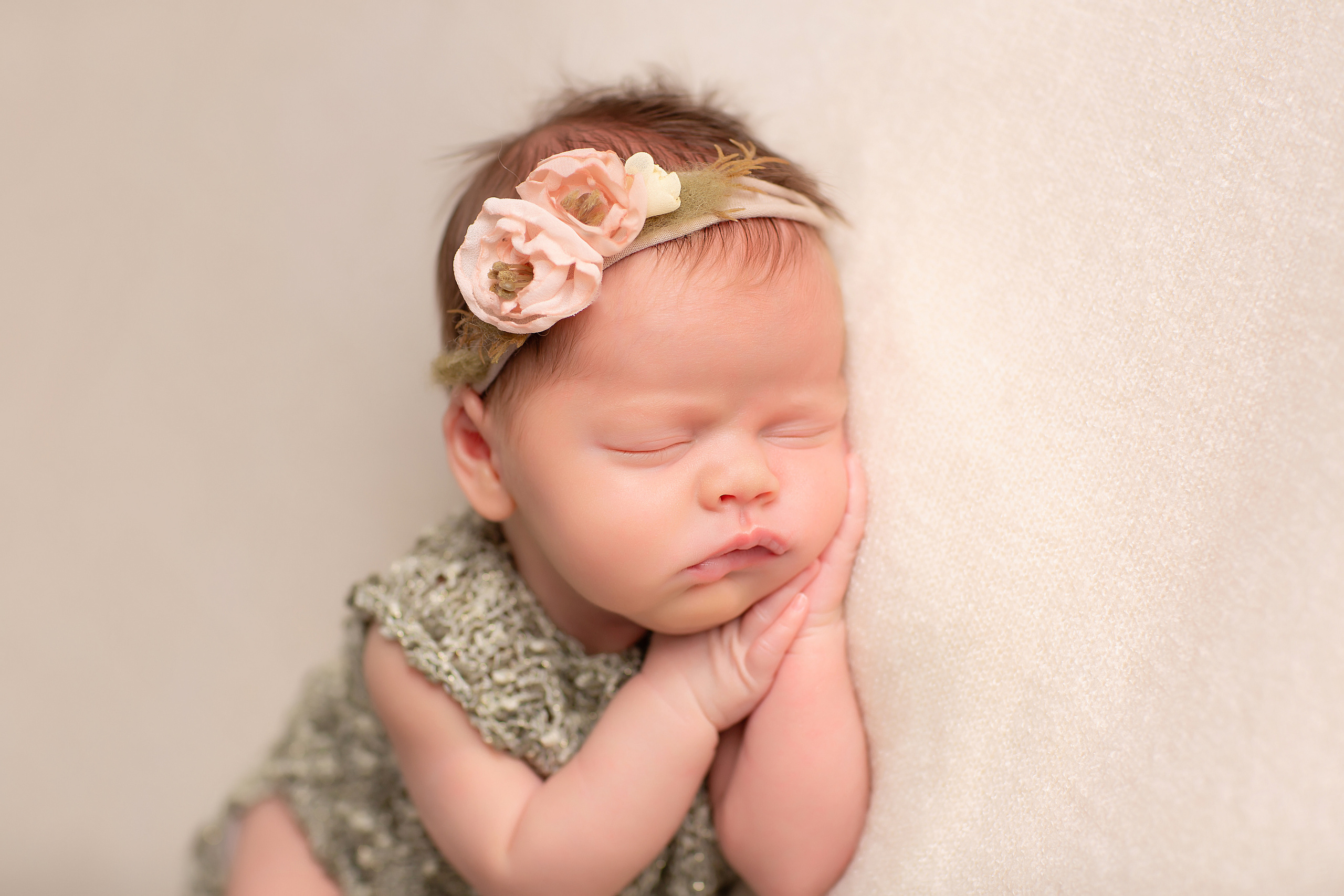новорожденная малышка в нежно-зеленом костюме и ободочком с цветами