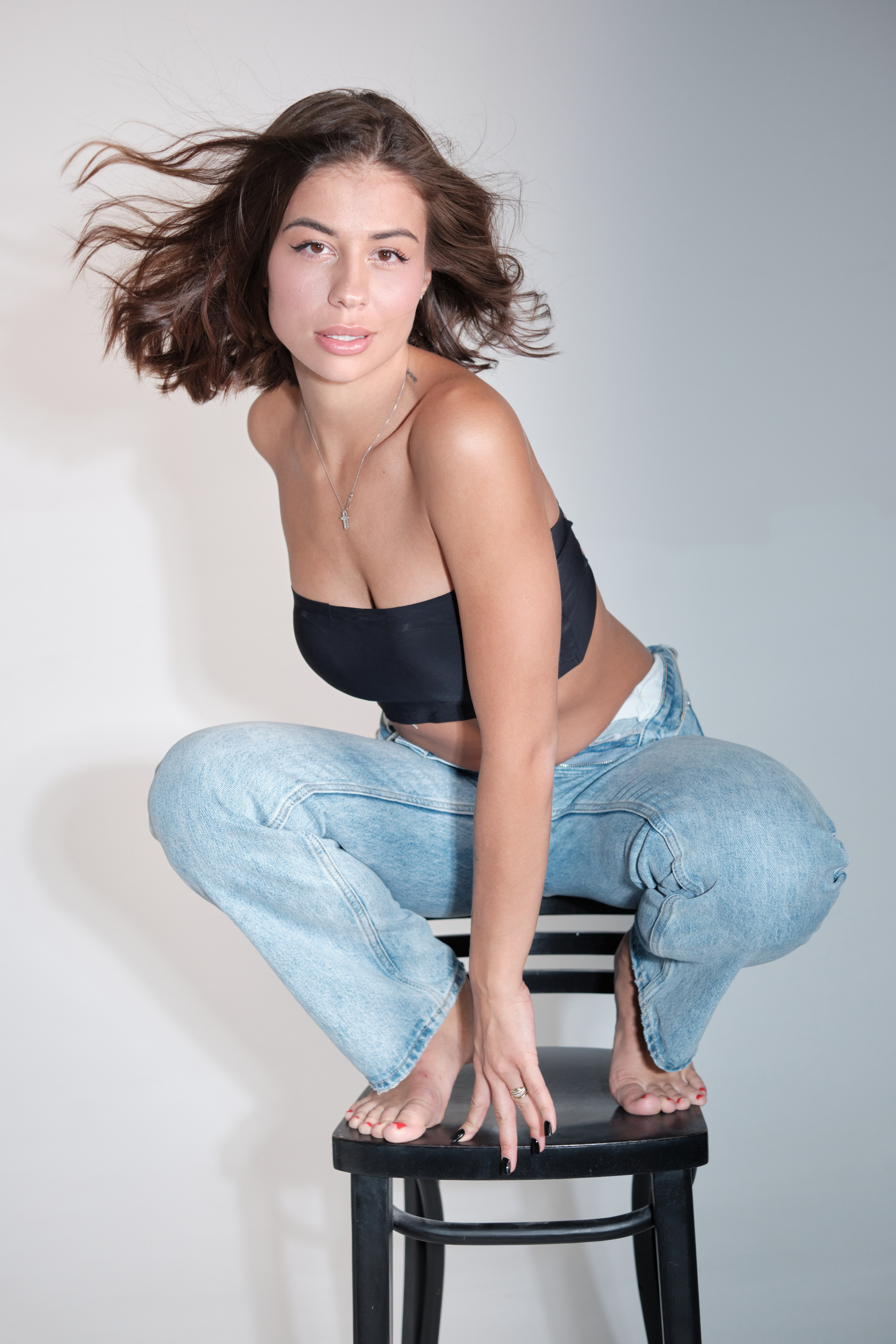 Сьемка в студии для модельного агентства, девушка в джинсах и черном топике стоит на стуле