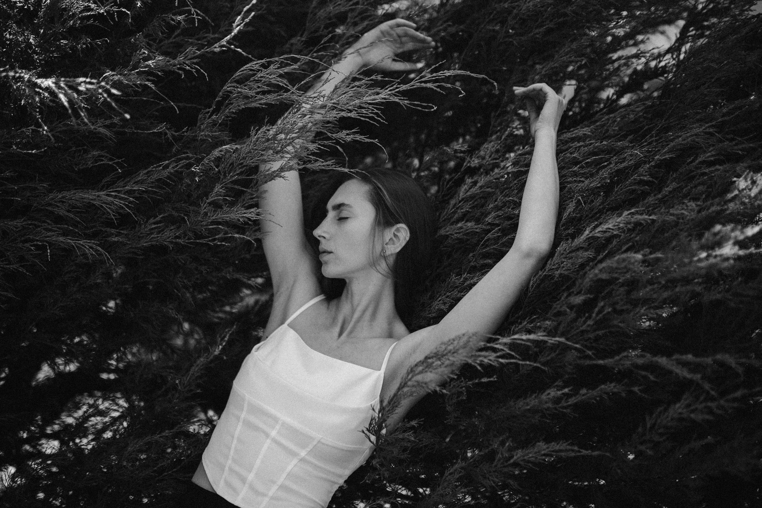 Девушка в белом корсете подняла руки на фоне дерева