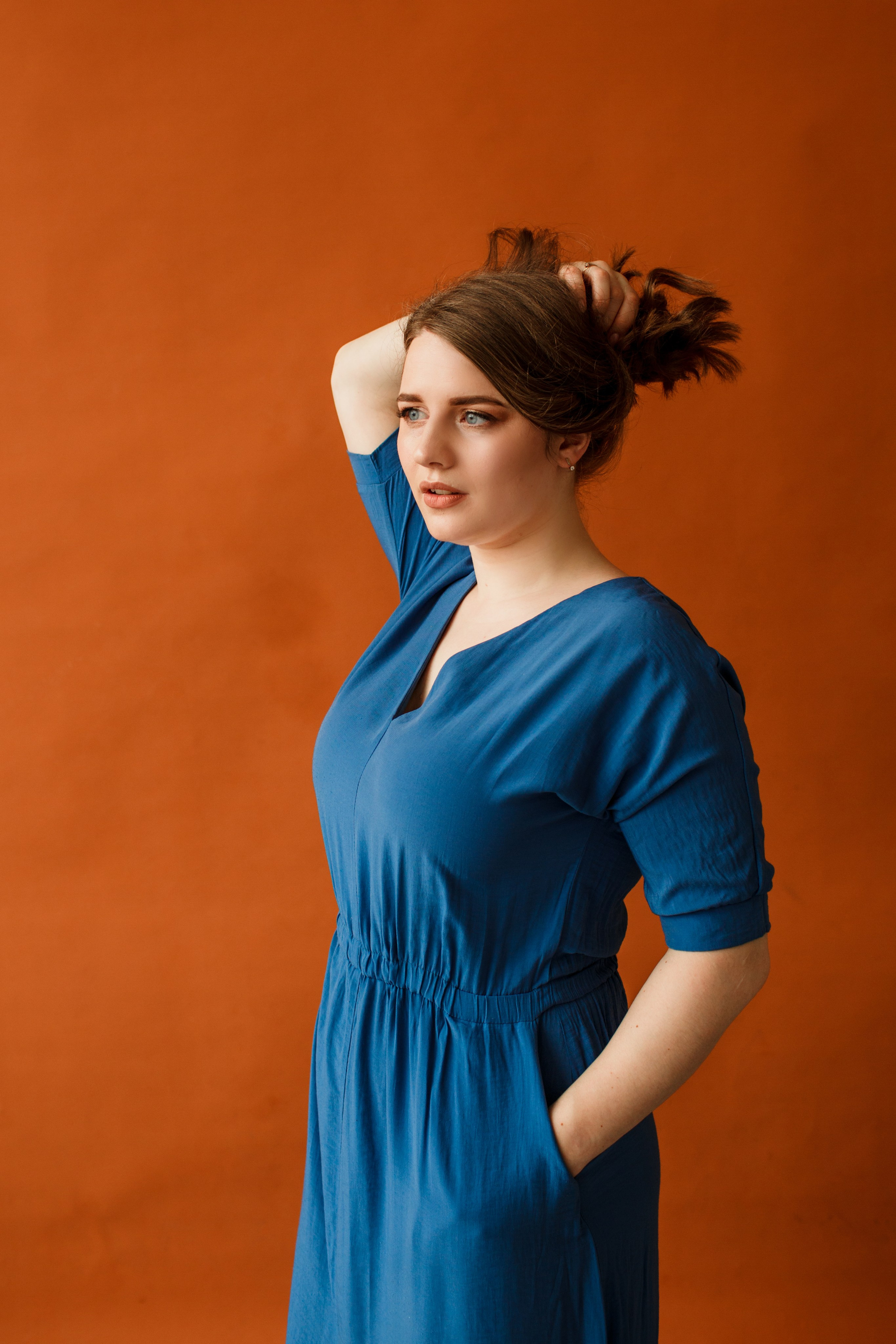 Девушка в синем платье позирует на фоне светло-коричневой стены.