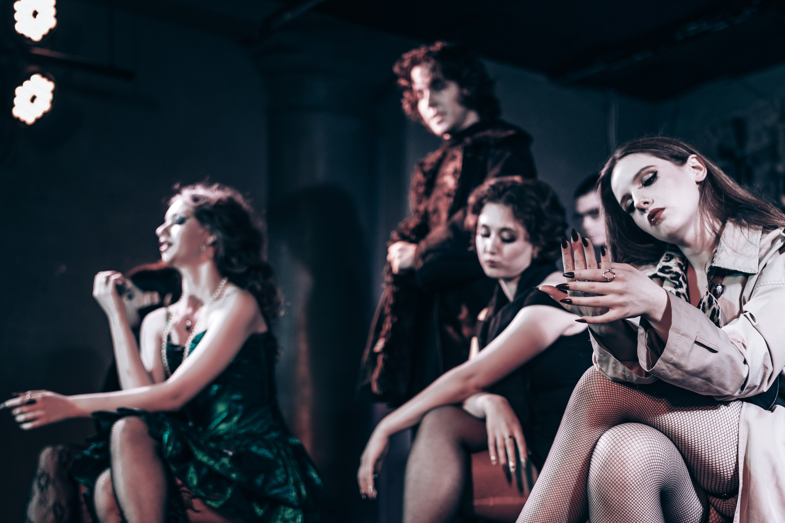 Девушки на сцене сидят на табуретах, парни ходят вокруг