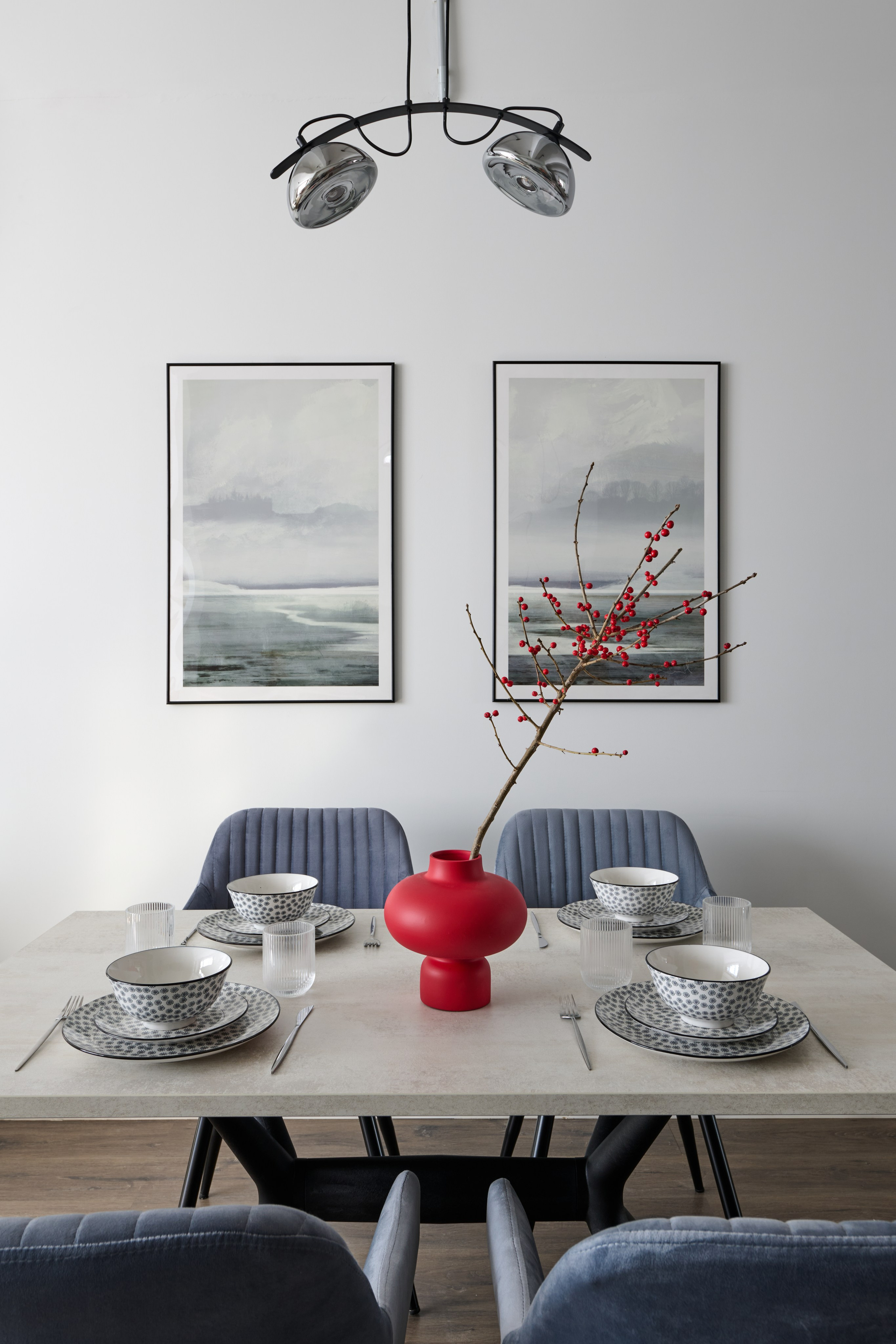 Крупный план обеденного стола с сервировкой для четырех человек. В центре стола - красная ваза с ветками красных ягод.