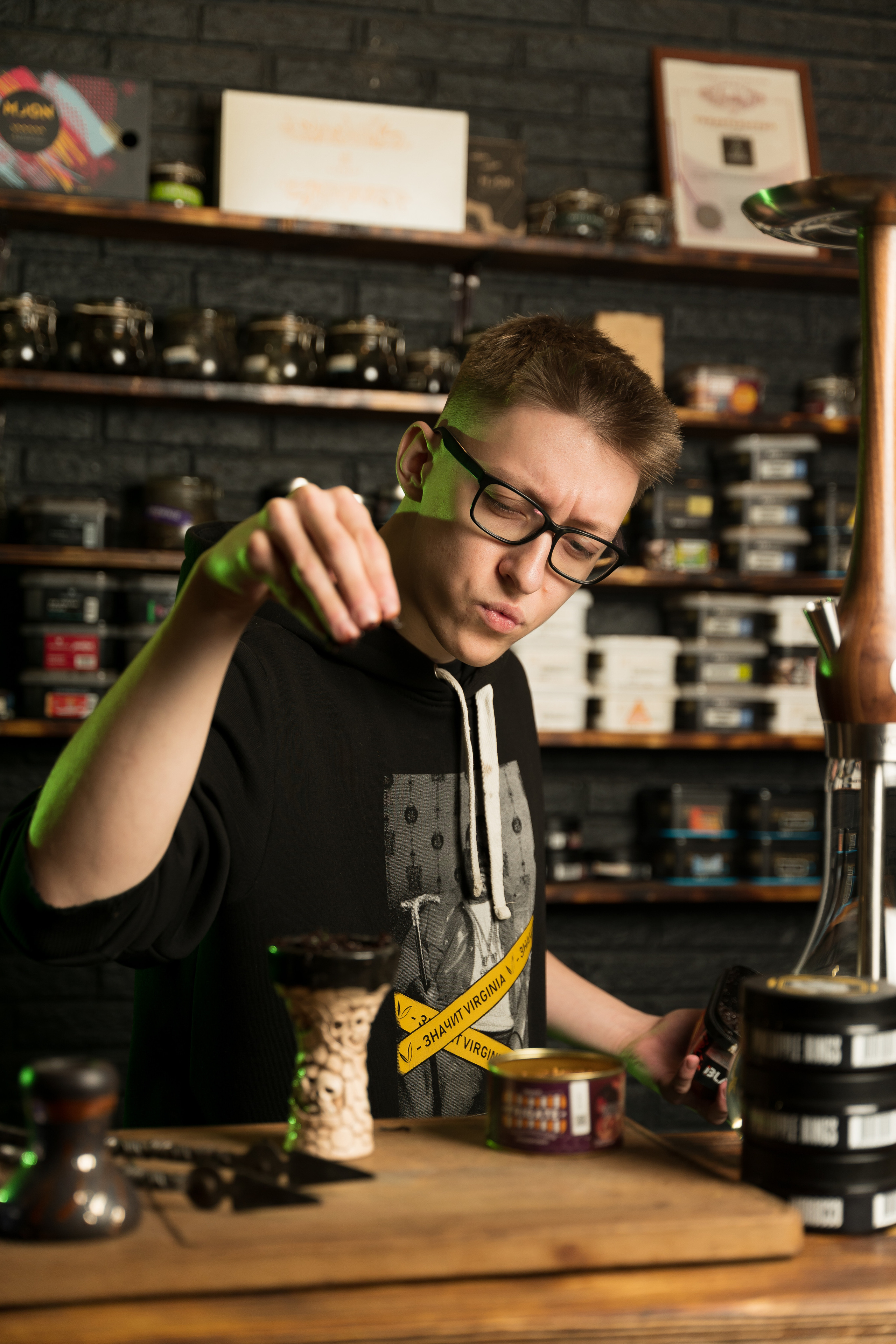 Family Community Нижний Новгород Фотосъемка персонала. Молодой человек мужчина парень кальянщик в очках готовит табак для кальяна в кальянной.