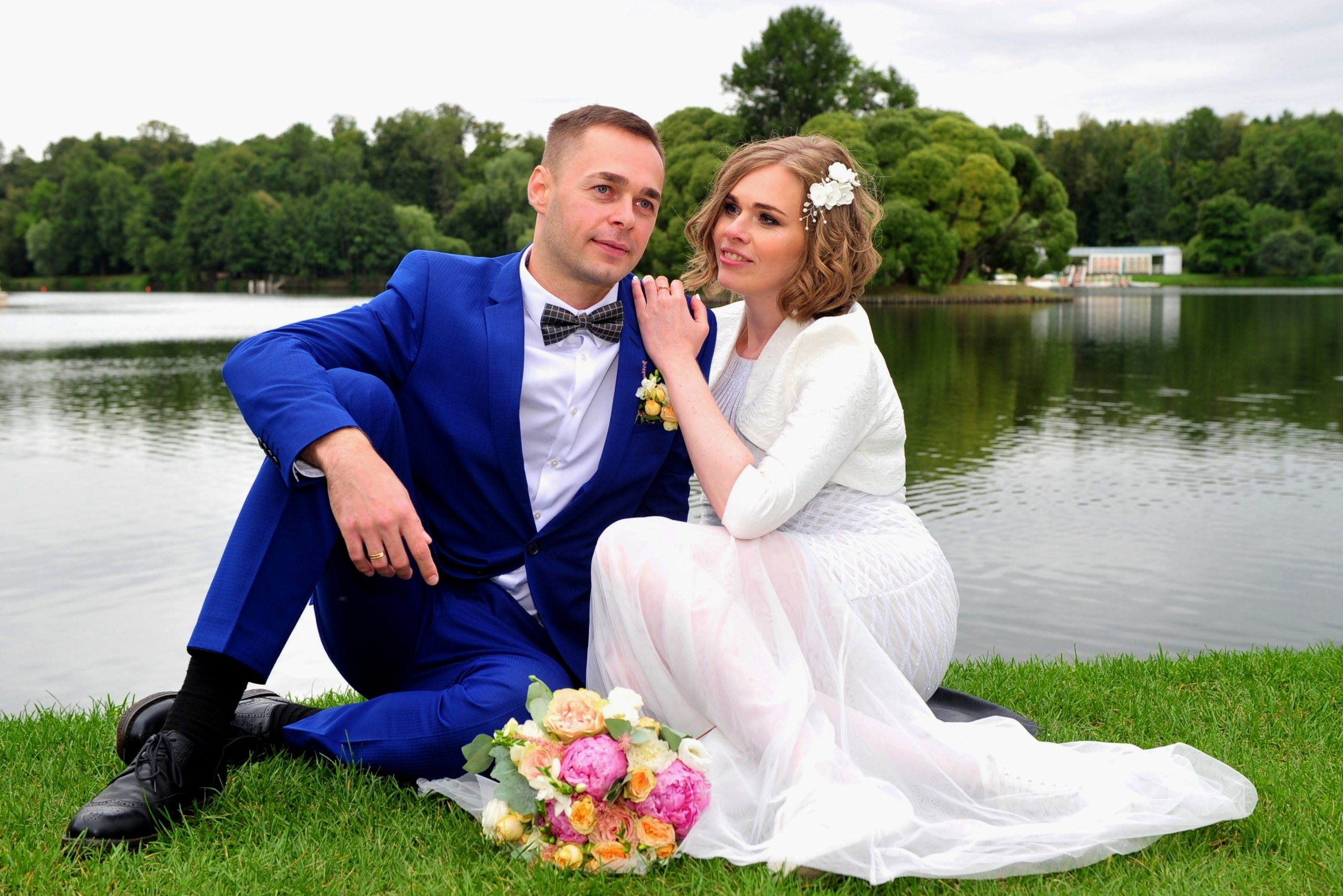 Свадьба в Царицыно хмурым прохладным летним днём, новобрачные сидят на траве на берегу пруда, невеста оперлась на плечо жениха
