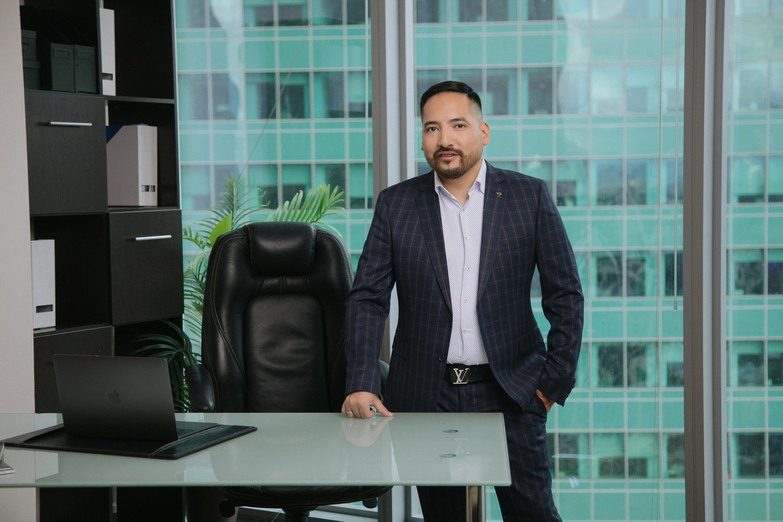 Мужчина в костюме позирует в офисе с панорамным видом на Москва-Сити.