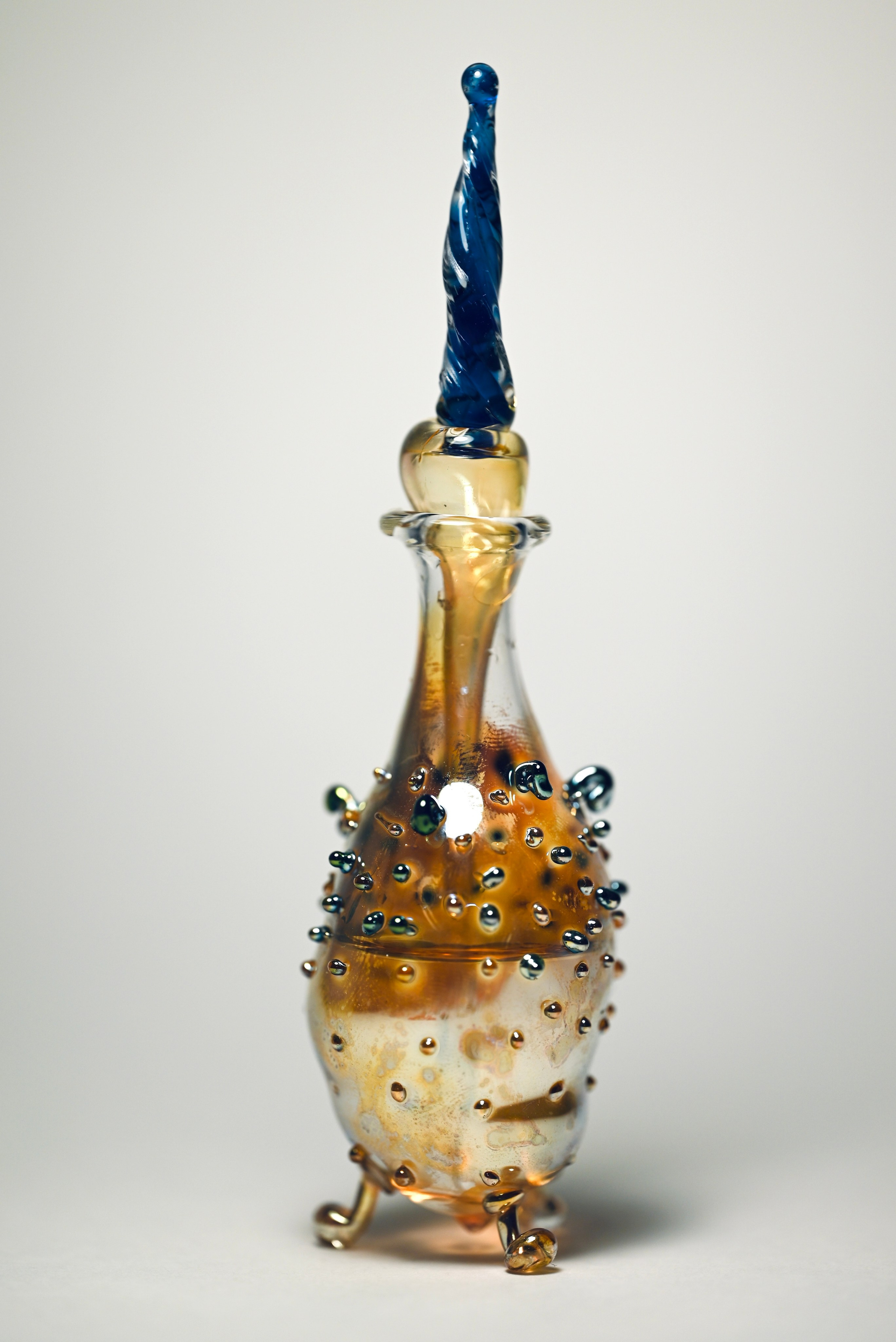 alt="Авторская стеклянная скульптура с прозрачной крышкой, янтарным корпусом и декоративными каплями на поверхности."