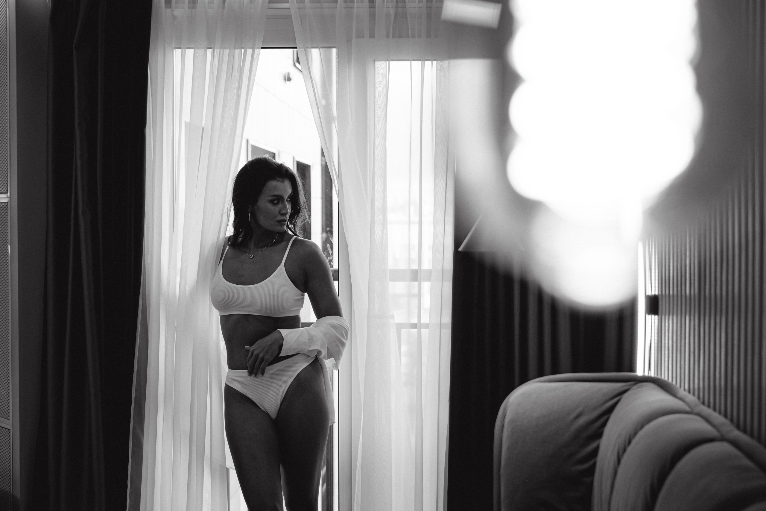 "Изящная дама в номере отеля, создает атмосферу расслабленности и роскоши в своем чарующем белье и непринужденной рубашке."