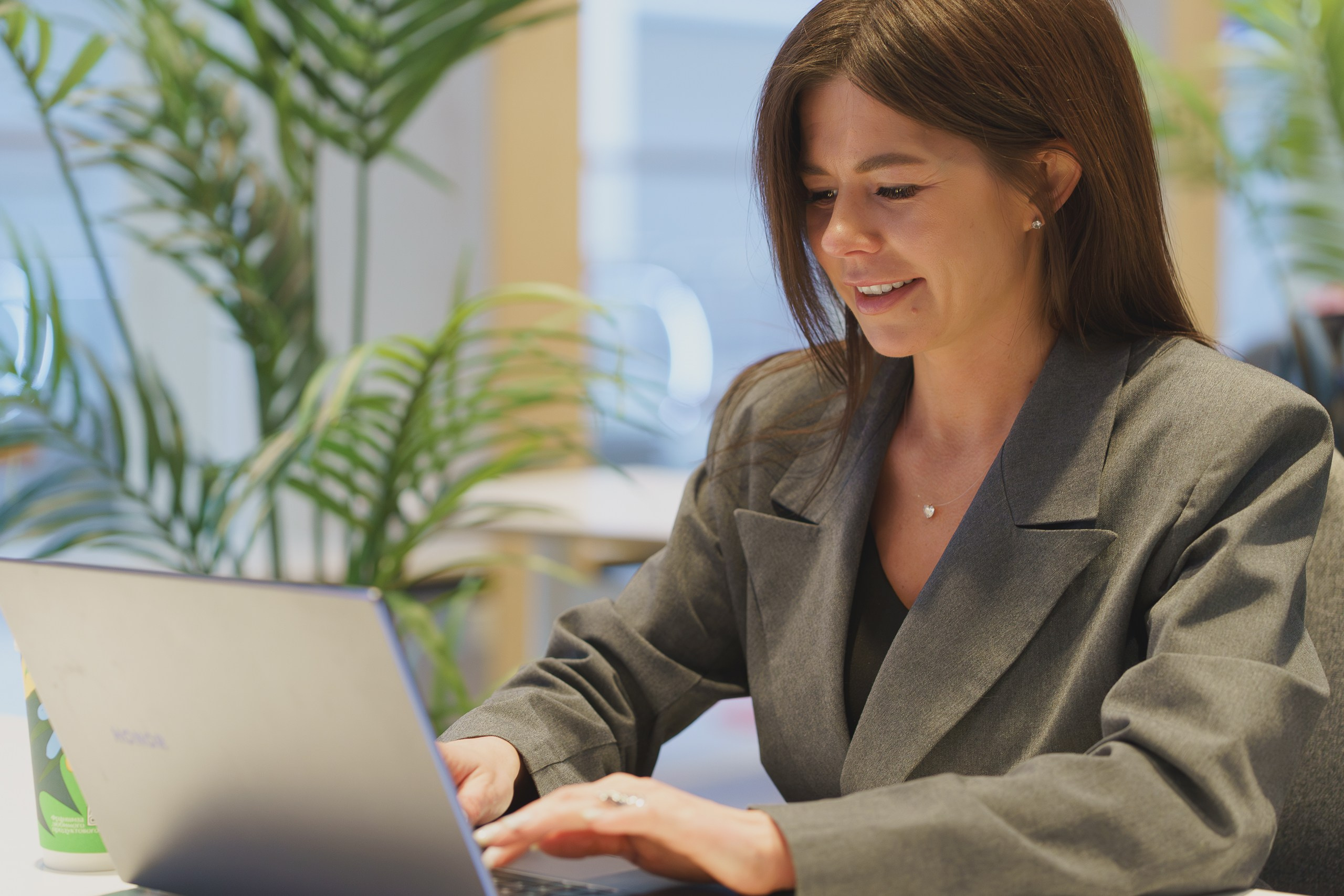 Дарья в костюме на фоне офисной обстановки, полупрофиль