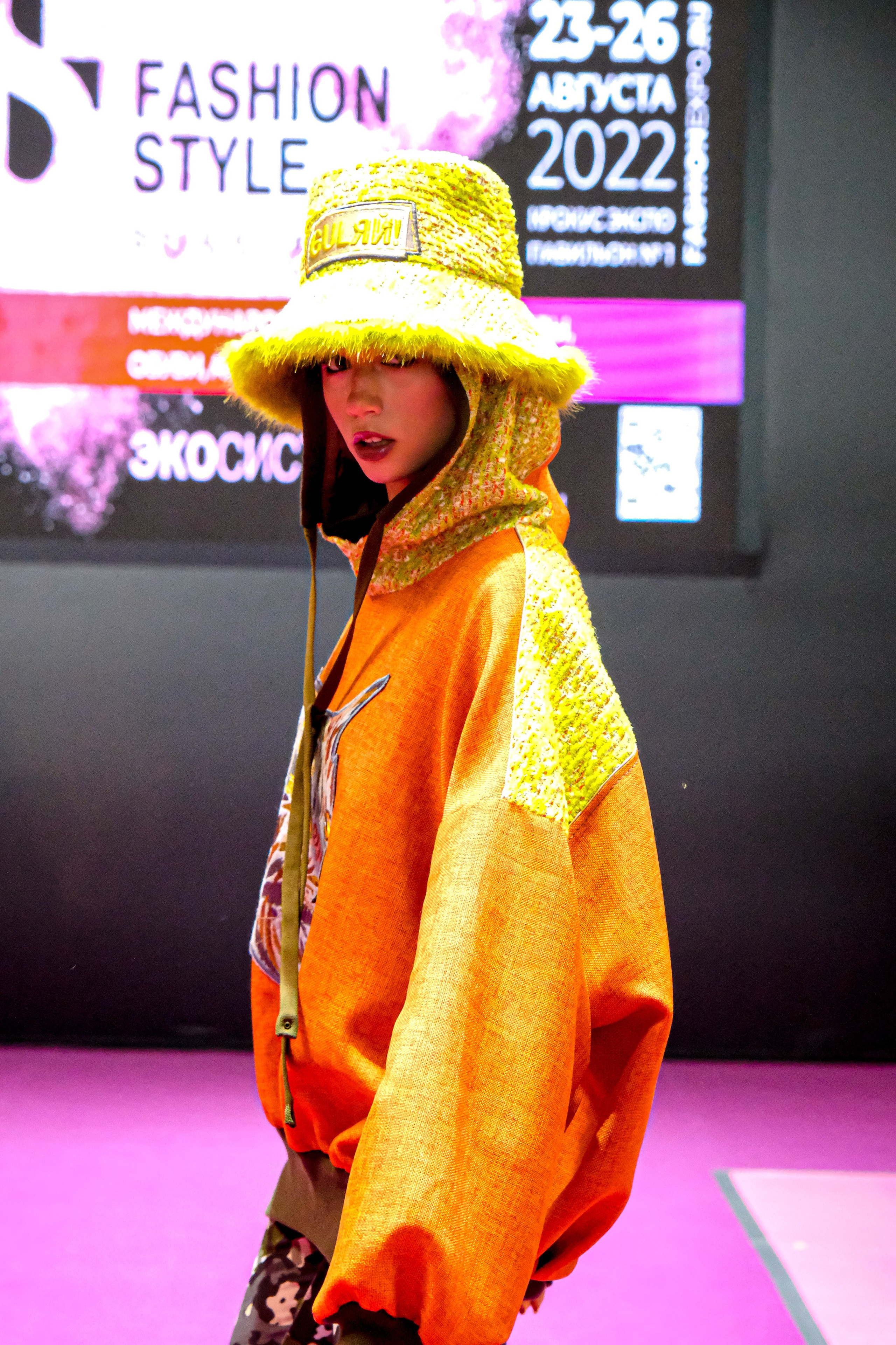  "Модели в ярких нарядах проходят по подиуму во время показа мод, освещенные яркими софитами и окруженные восторженными зрителями."