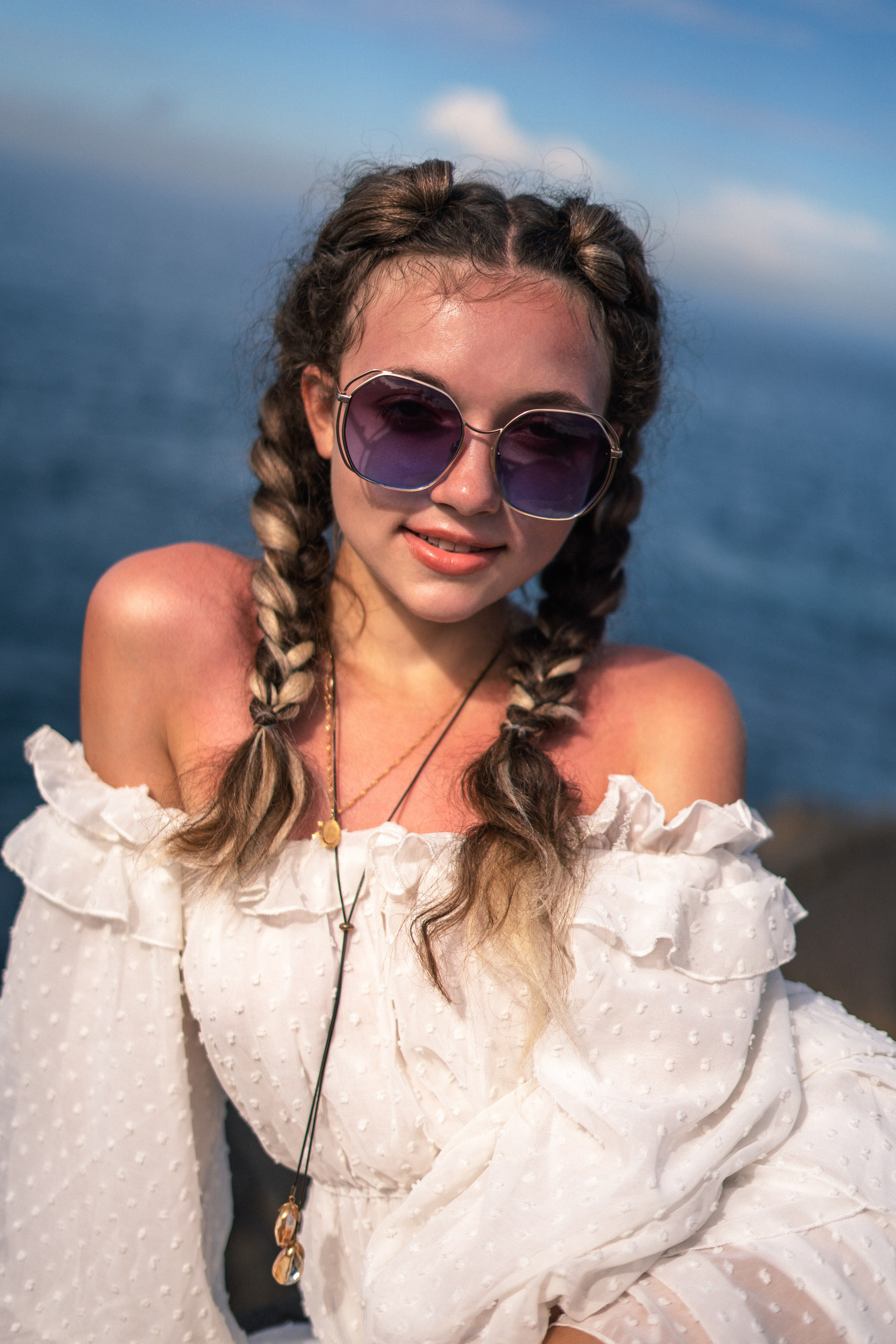 a girl in a white dress and glasses with a joyful expression on her face on the rocks by the ocean