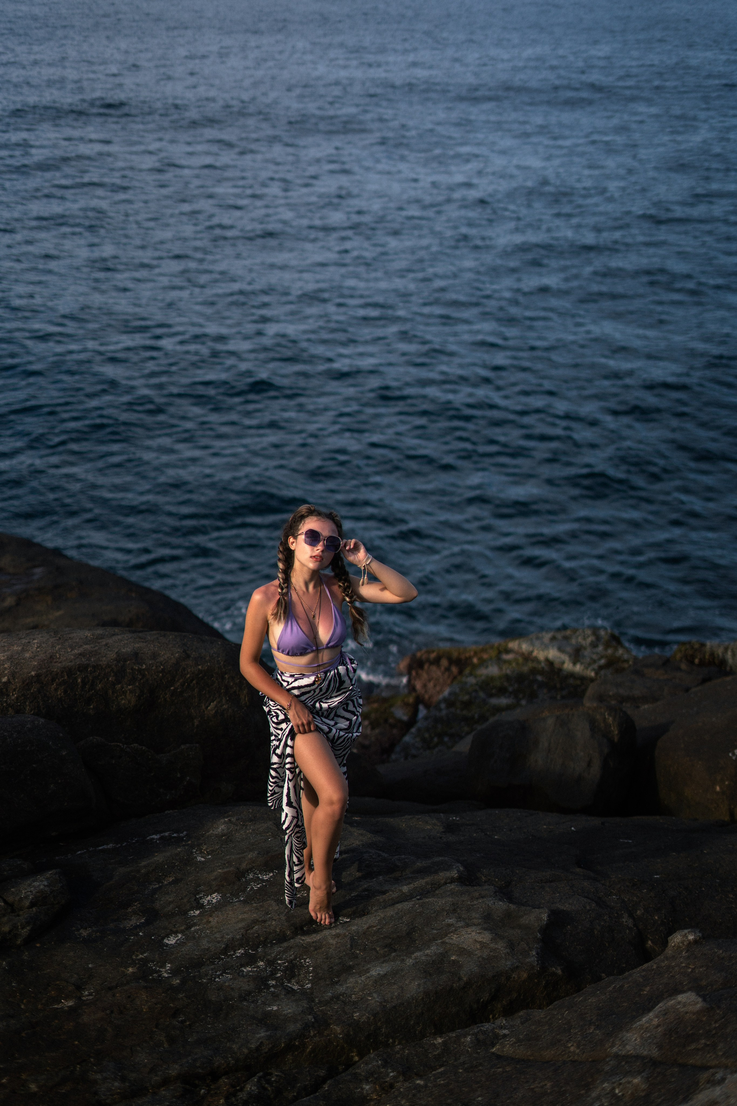 a young beauty in a purple swimsuit with a smiling face on the rocks