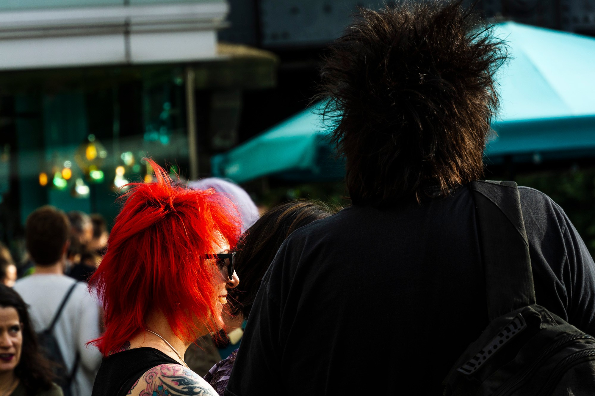 Крупный план женщины с ярко-рыжими волосами и мужчины с высоким черным ирокезом на городской улице.