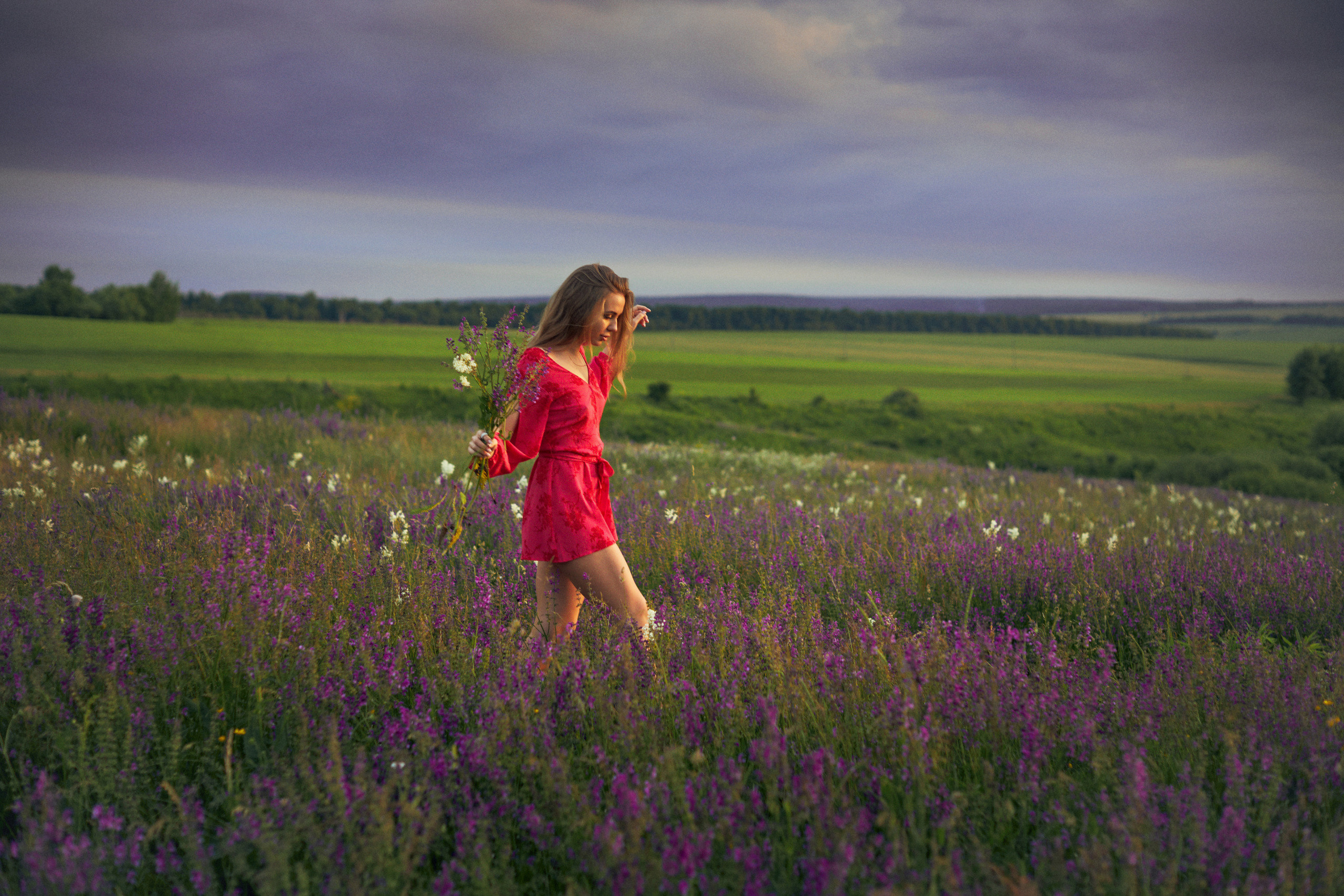 Девушка в коротком красном комбинезоне гуляет по цветочному полю