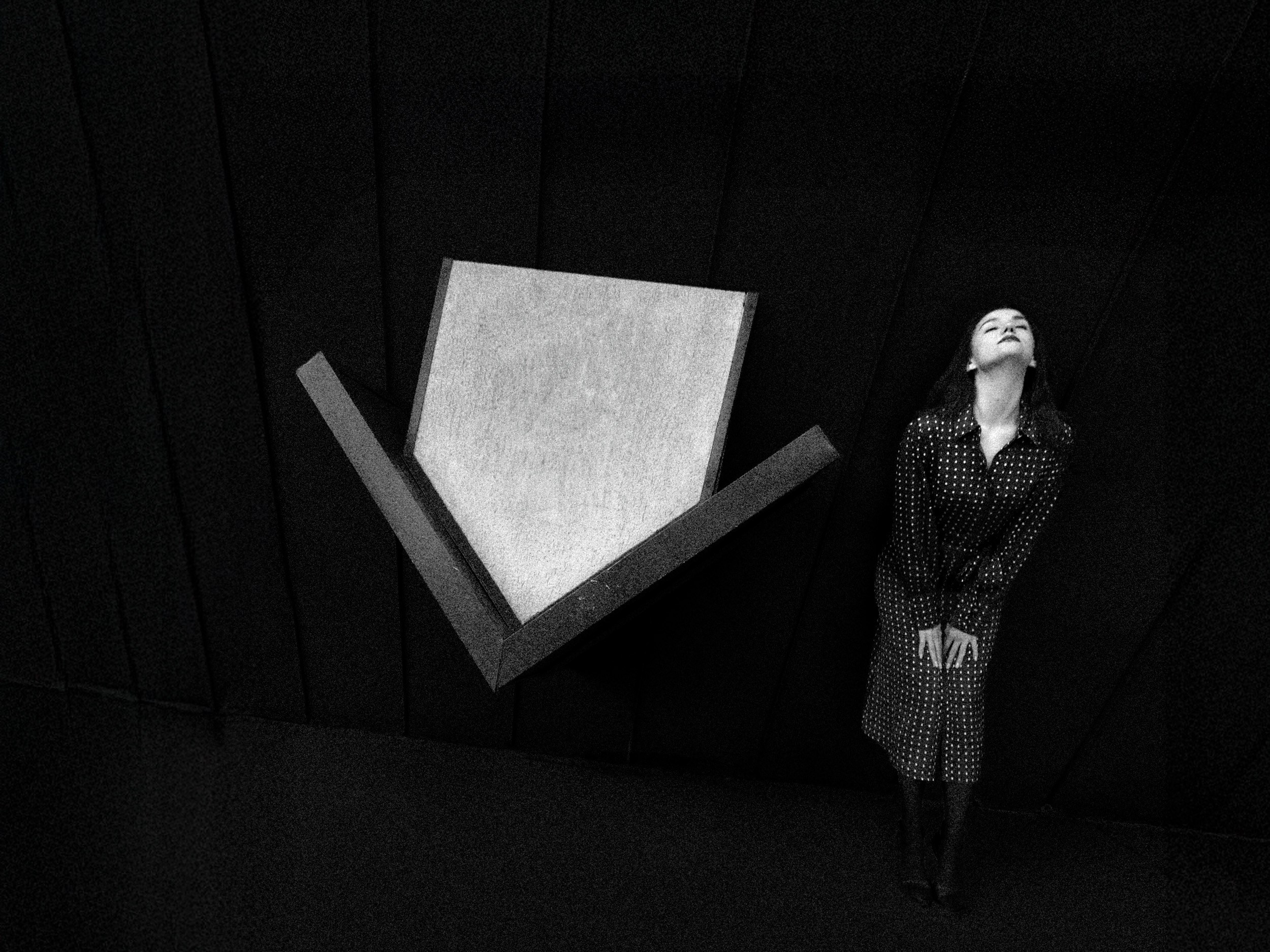 Чёрно-белая фотография женщины в платье в горошек у геометрической инсталляции на тёмном фоне