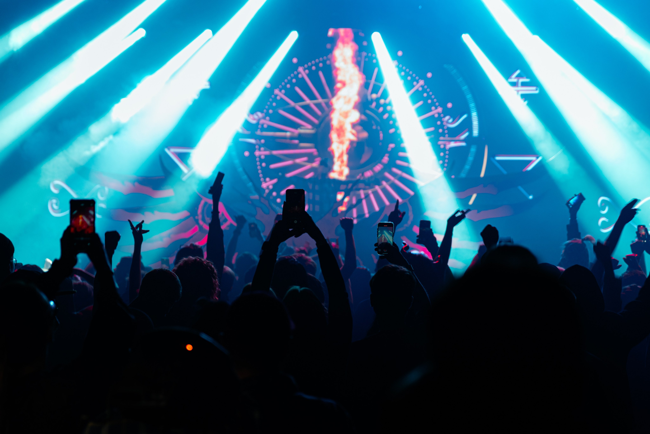 Концерт, фото из зала, лучи светят со сцены на толпу, зрители поднимают руки вверх