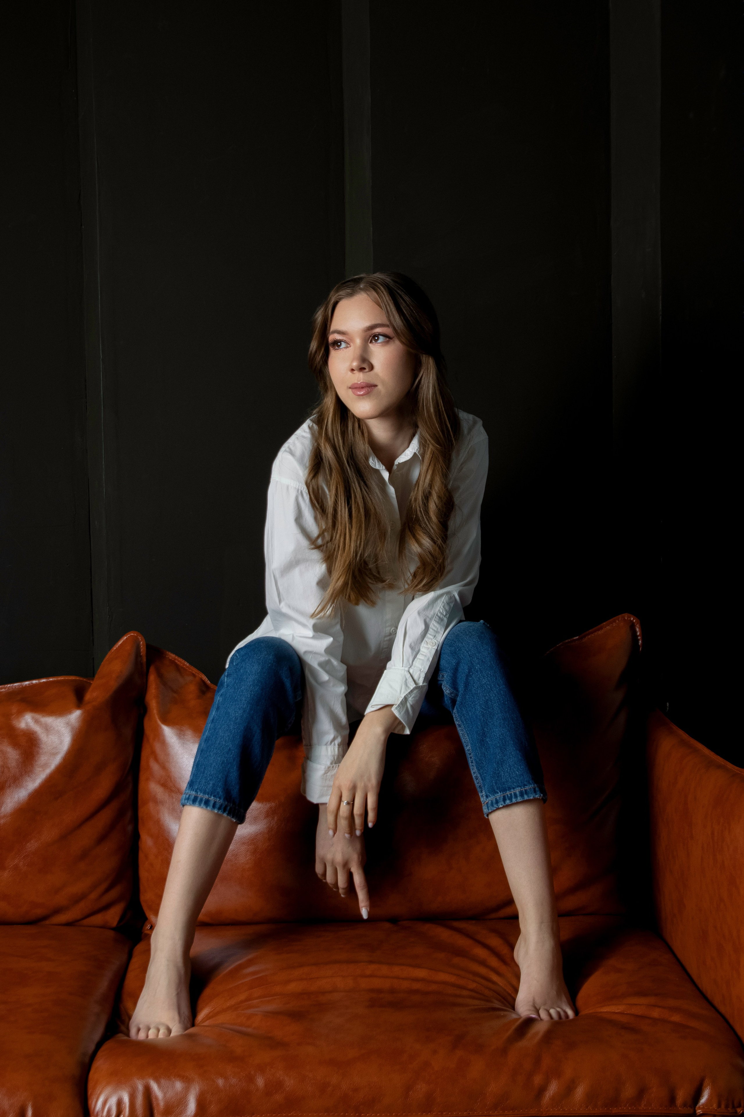 Девушка сидит на диване в джинсах и белой рубашке