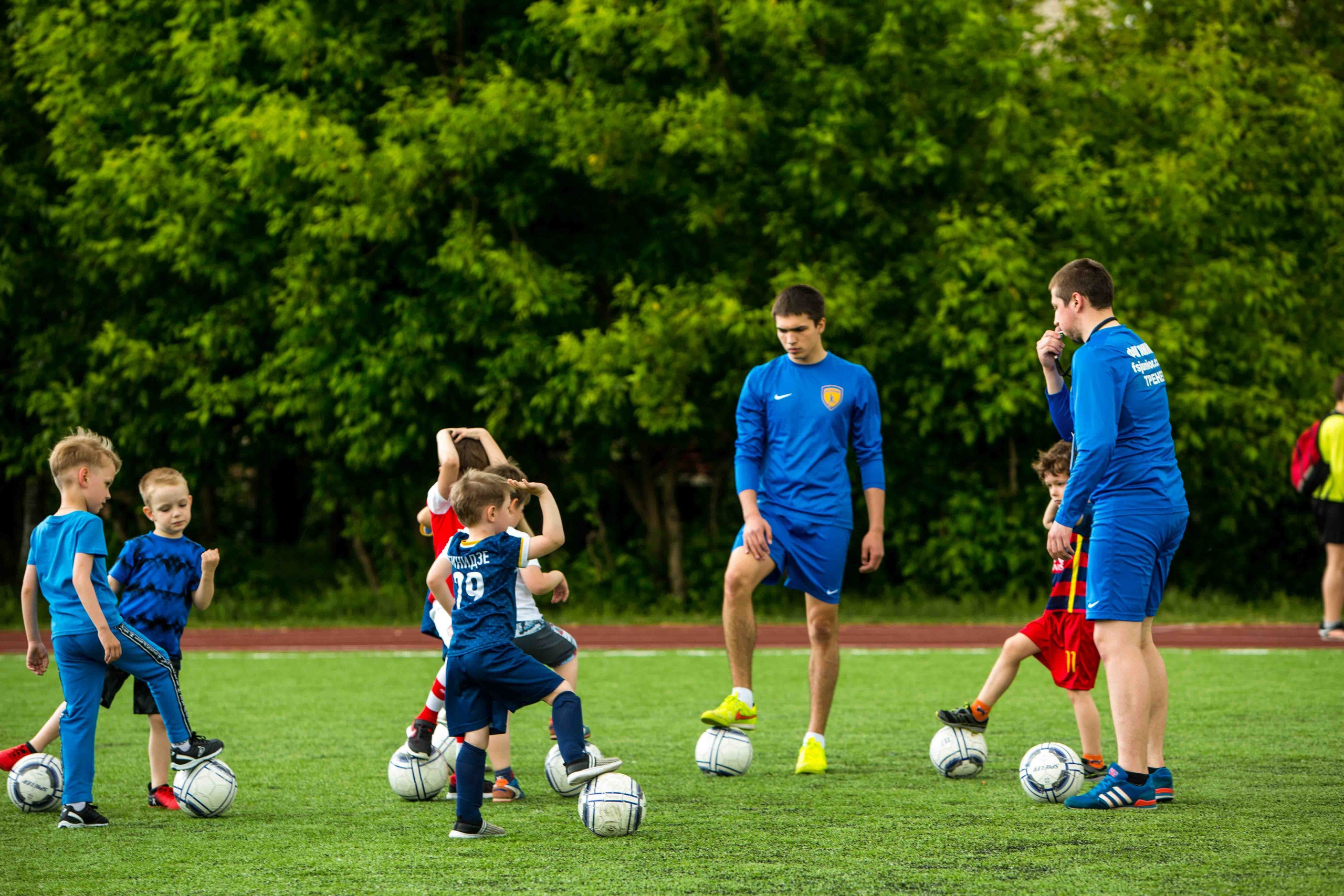 Дети играют в футбол на поле с тренером, командная работа