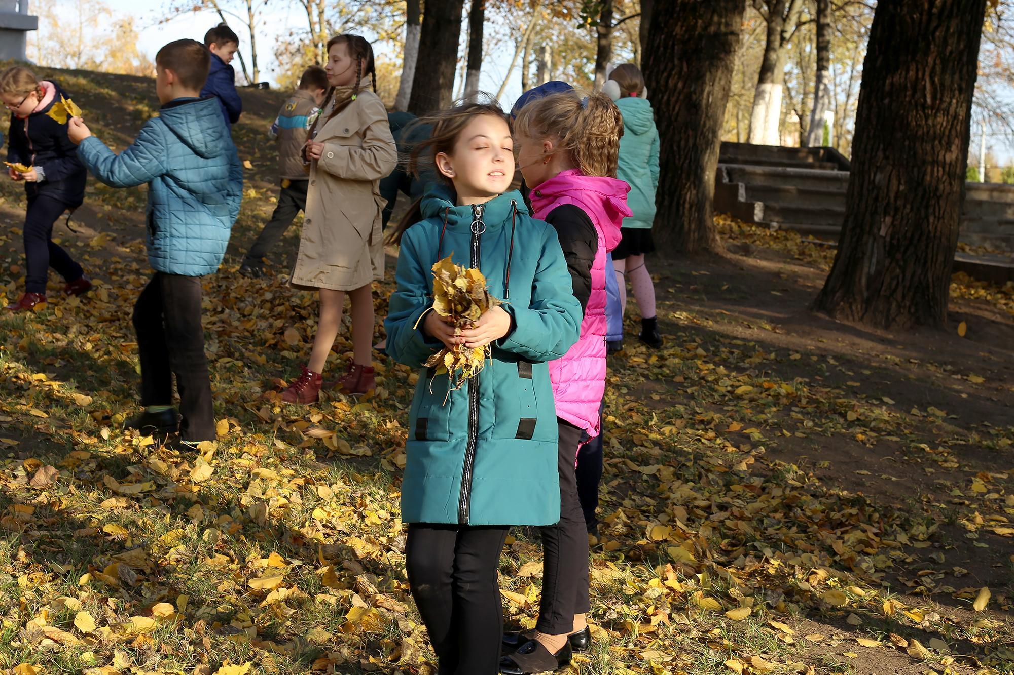 девочка в зеленой куртке подбрасывает листья