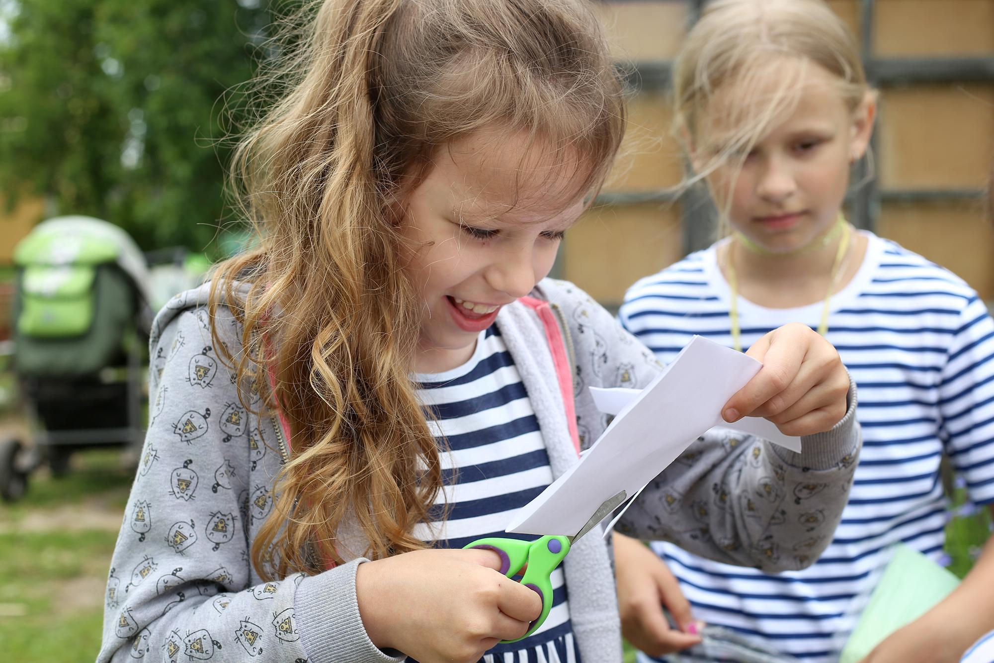 девочка в полосатой майке разрезает белый лист