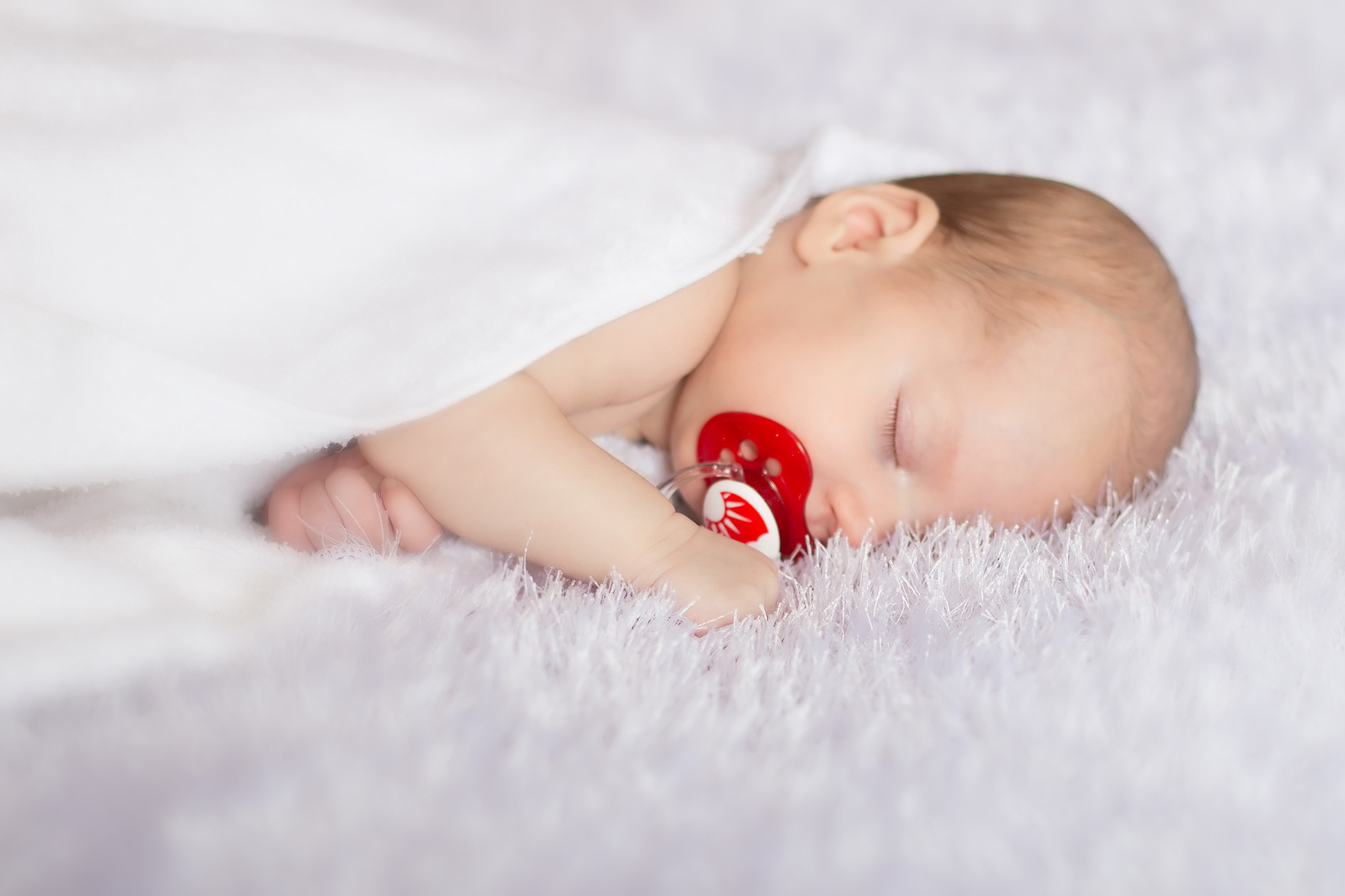 младенец в белом с красной пустышкой во рту