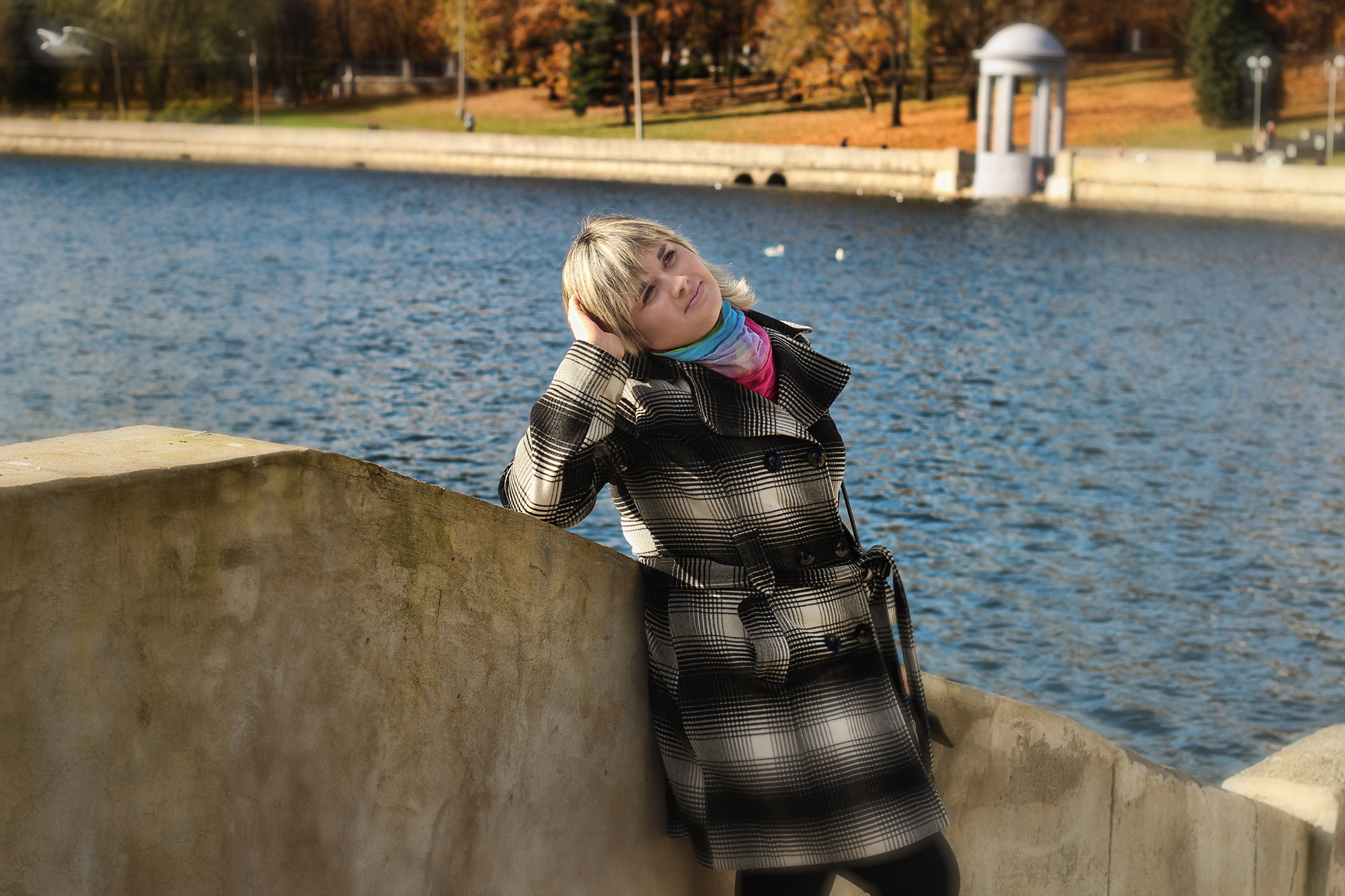 девушка в пальто гуляет по набережной в солнечный день