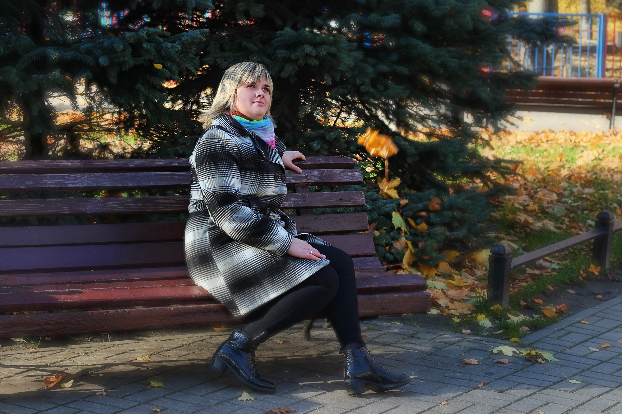 женщина в осеннем пальто в клетку сидит на скамейке