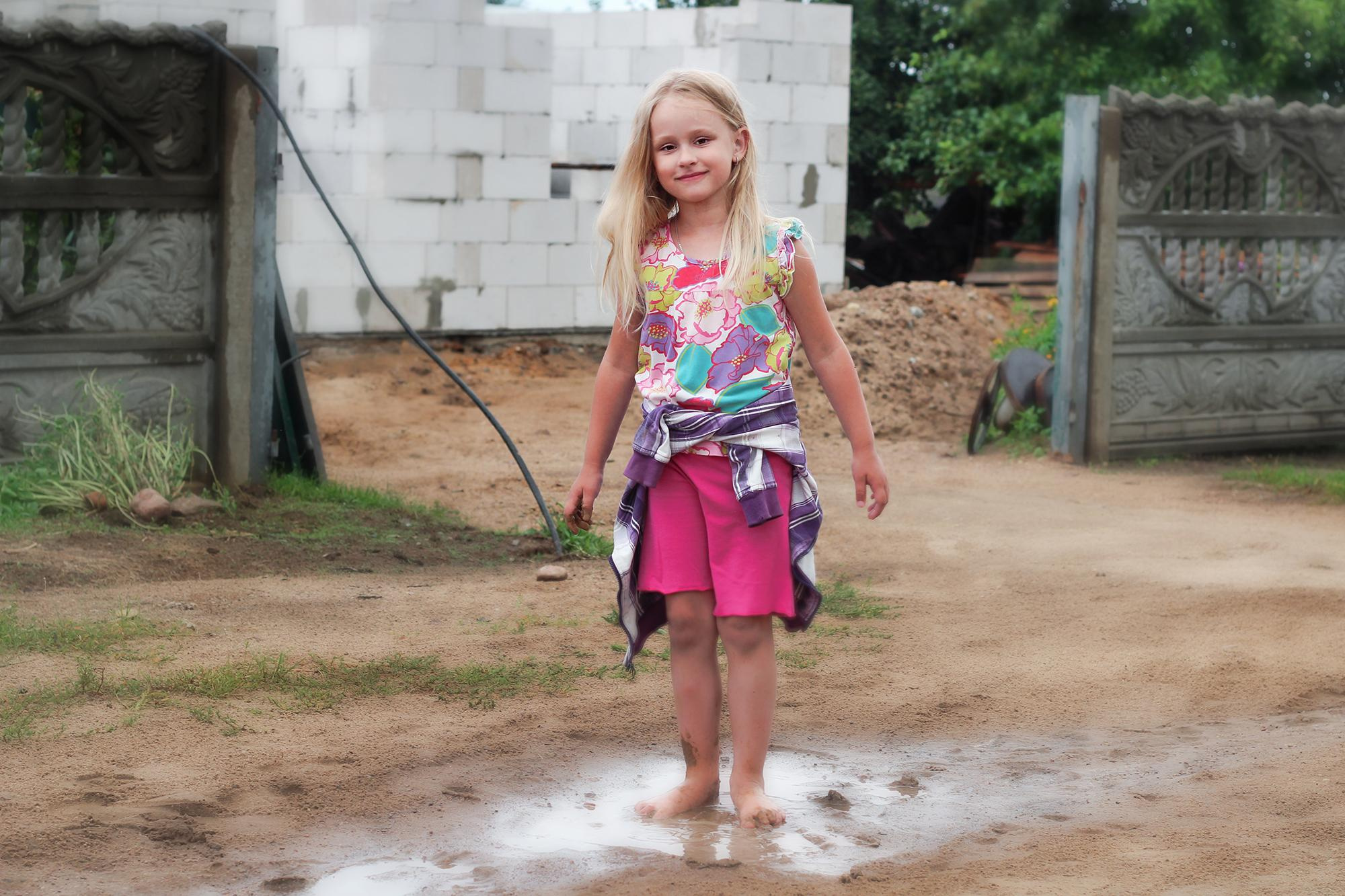 лохматая девочка стоит в грязной луже на деревенской дороге