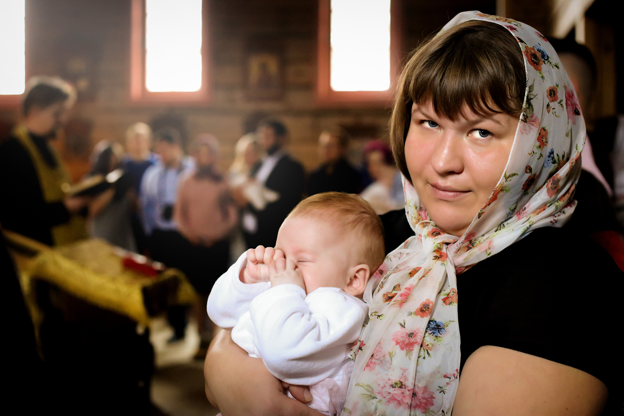 крестная мама держит ребенка на руках в церкви во время крещения