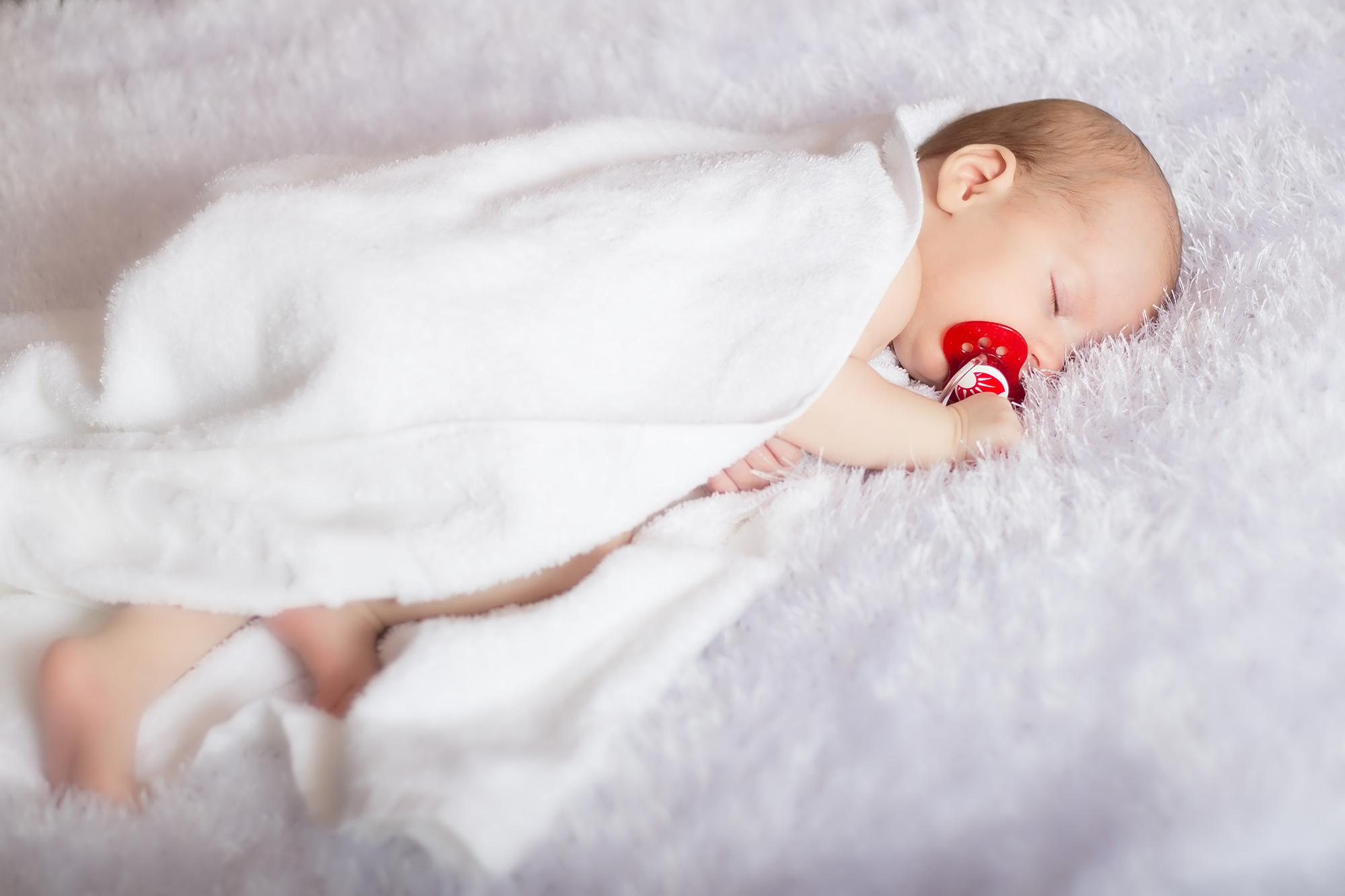 малыш спит  в белом полотенце с красной пустышкой