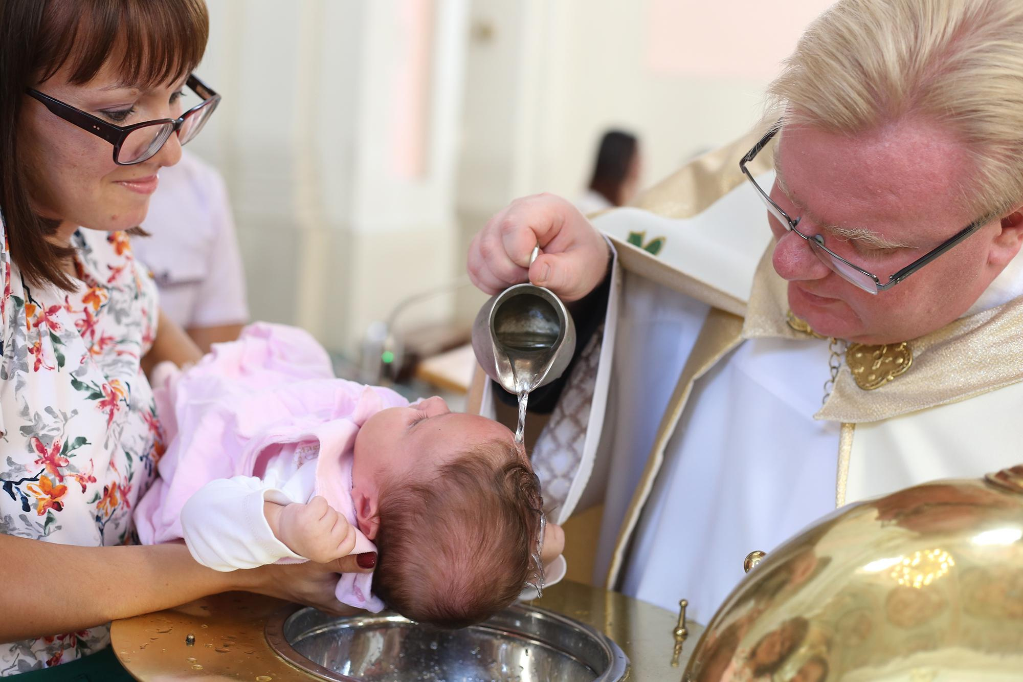 мама держит ребенка на руках во время крещения