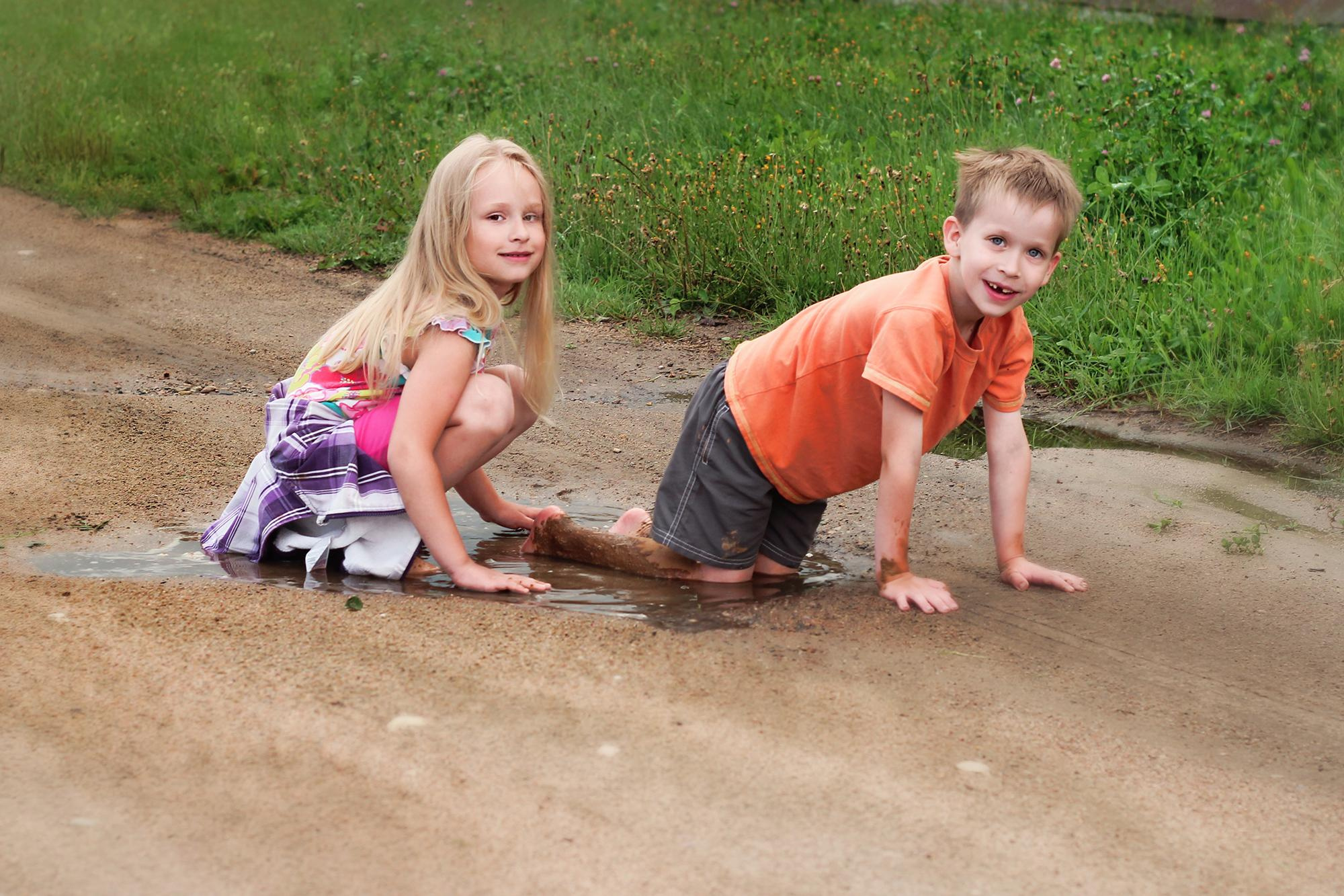 девочка и мальчик сидят в луже после дождя