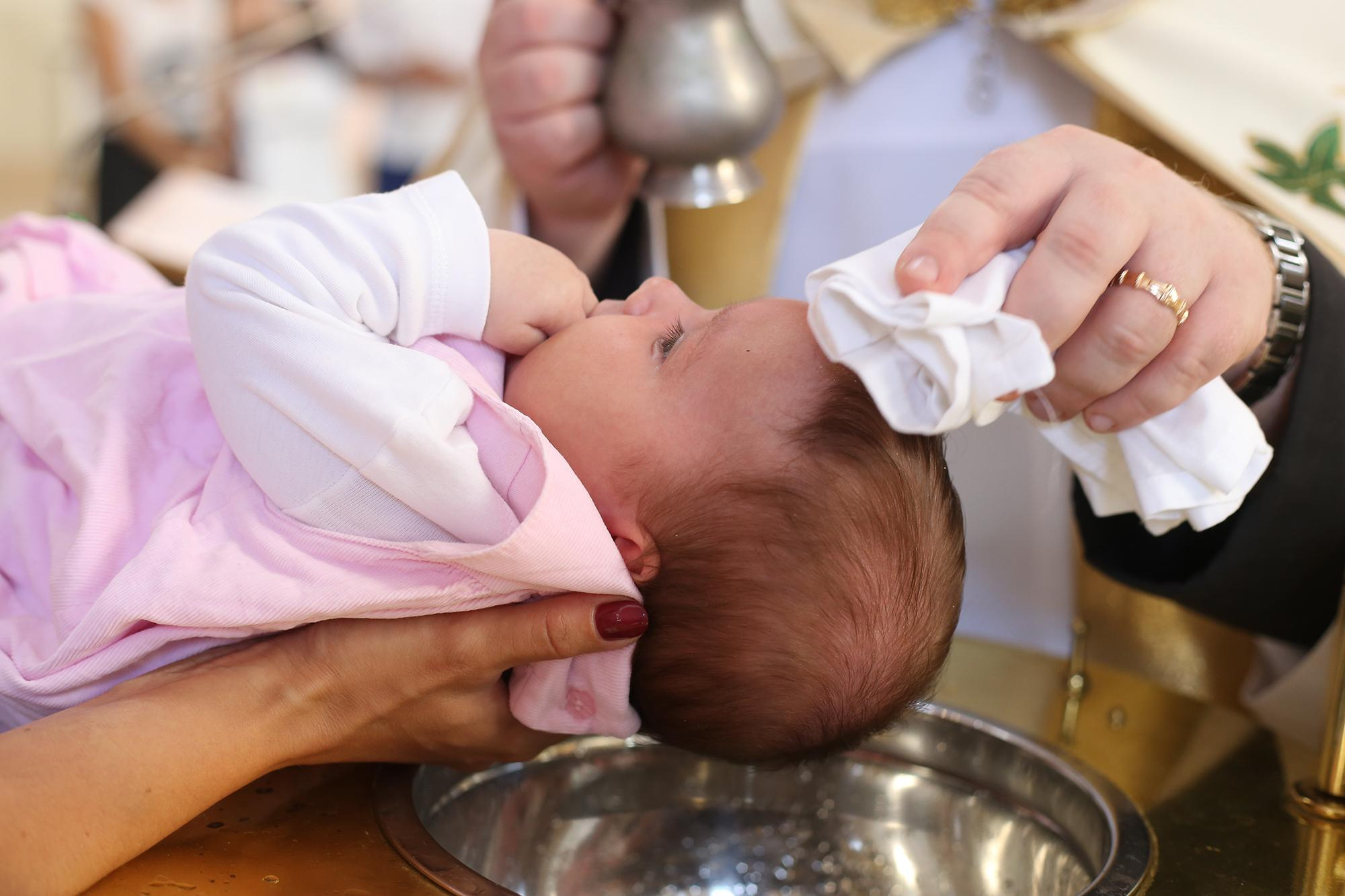 поп трогает лоб младенца во время крещения в костеле