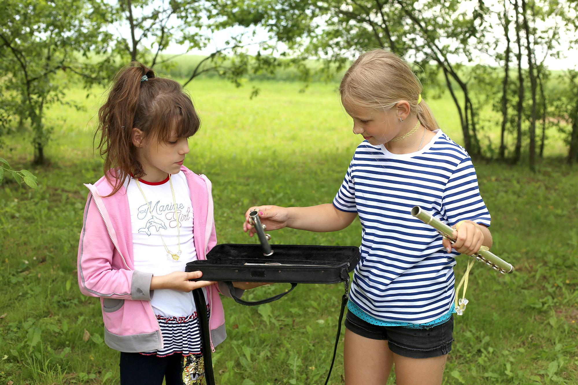 девочка в полосатой майке собирает флейту, на улице