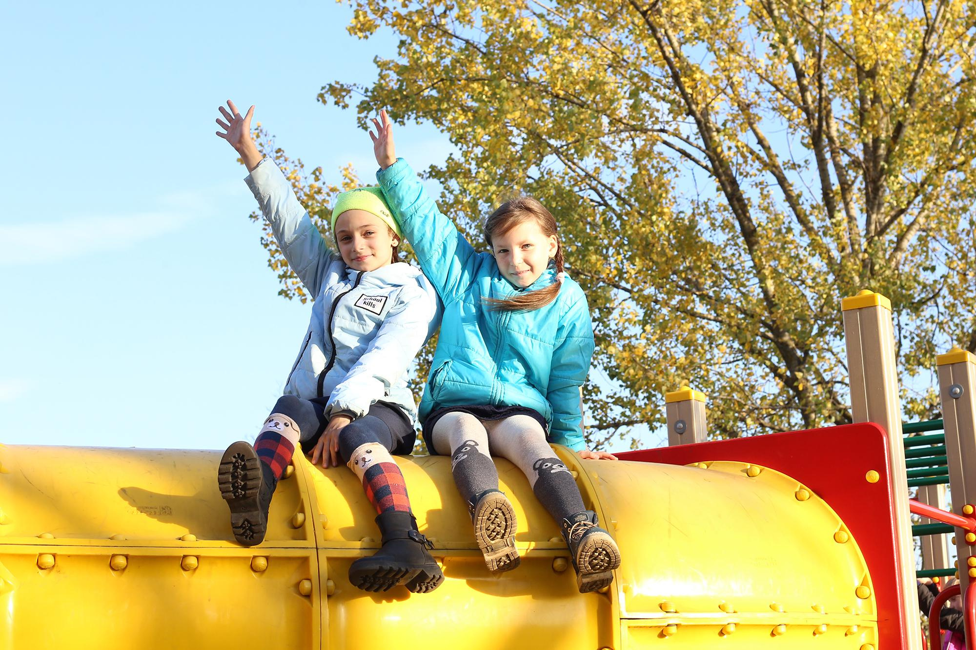 девочки машут руками сидя на горке в парке