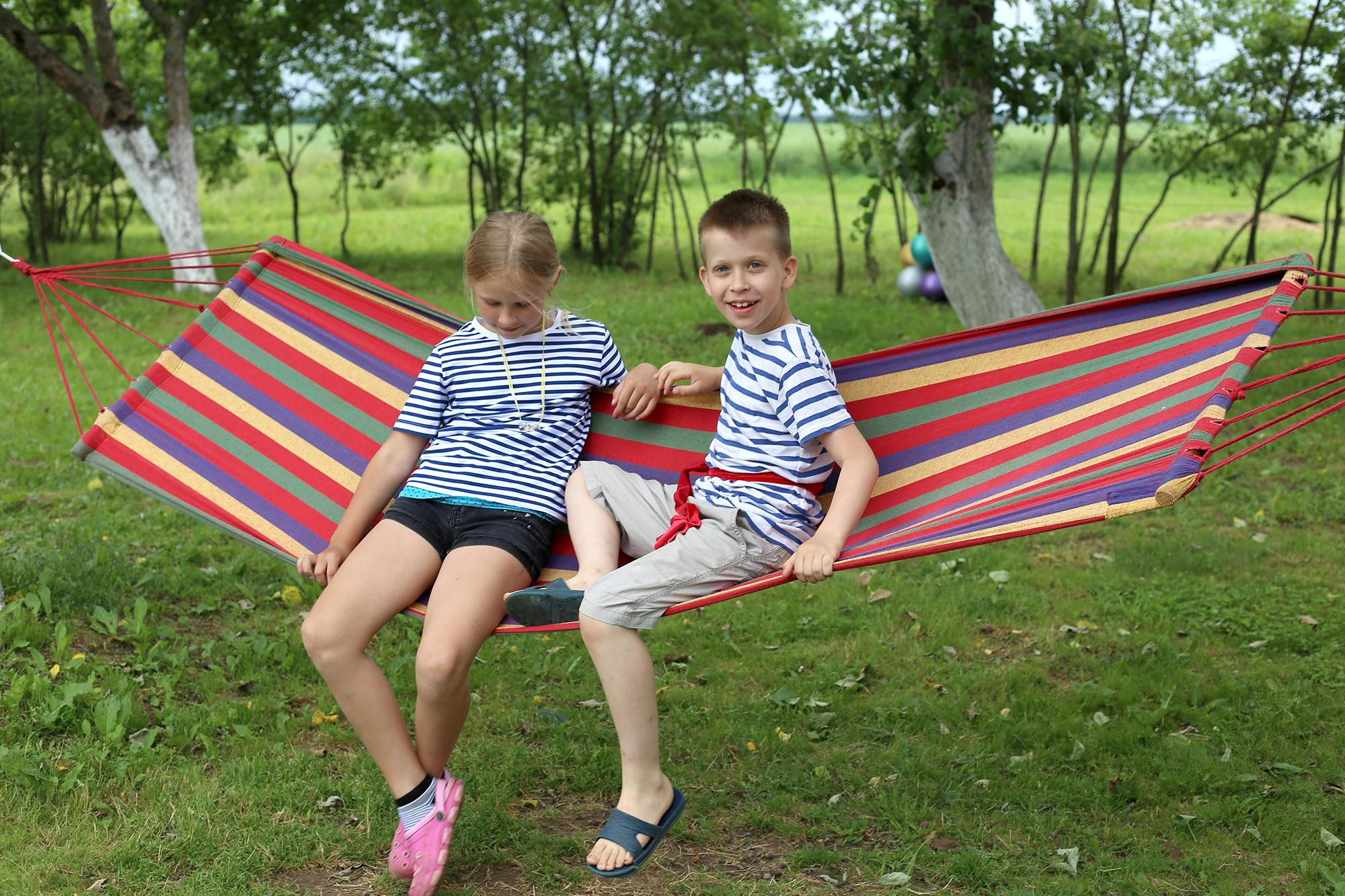 мальчик и девочка качаются на полосатом гамаке