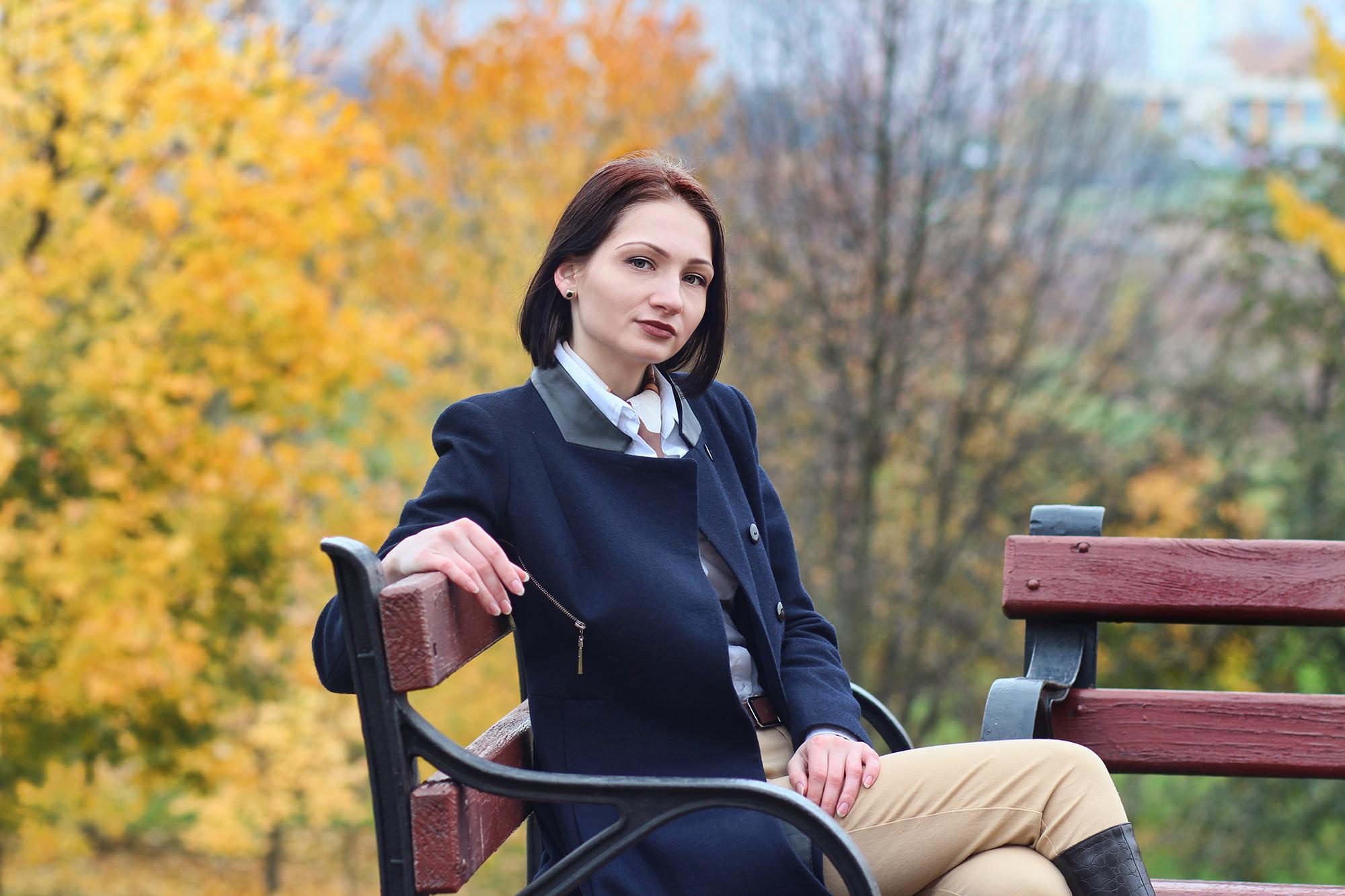 красивая леди сидит на деревянной скамейке в осеннем парке
