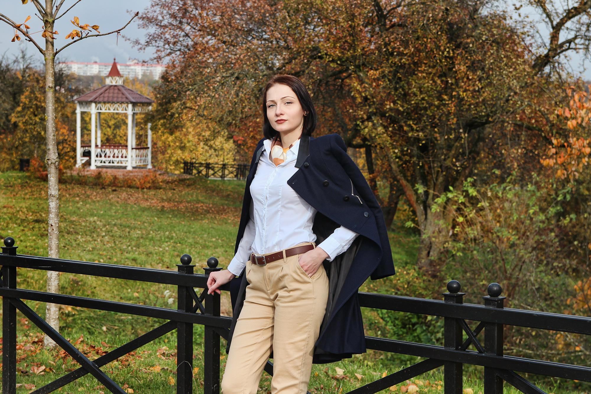 молодая женщина в песочных брюках оперлась на черный поручень