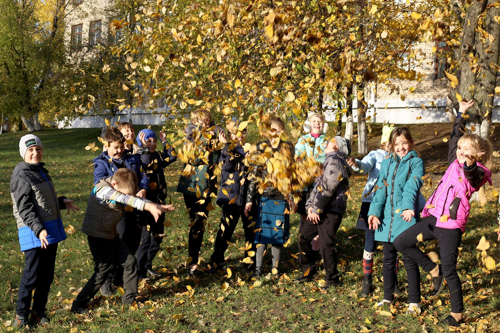школьники подбрасывают осеннюю листву во дворе школы
