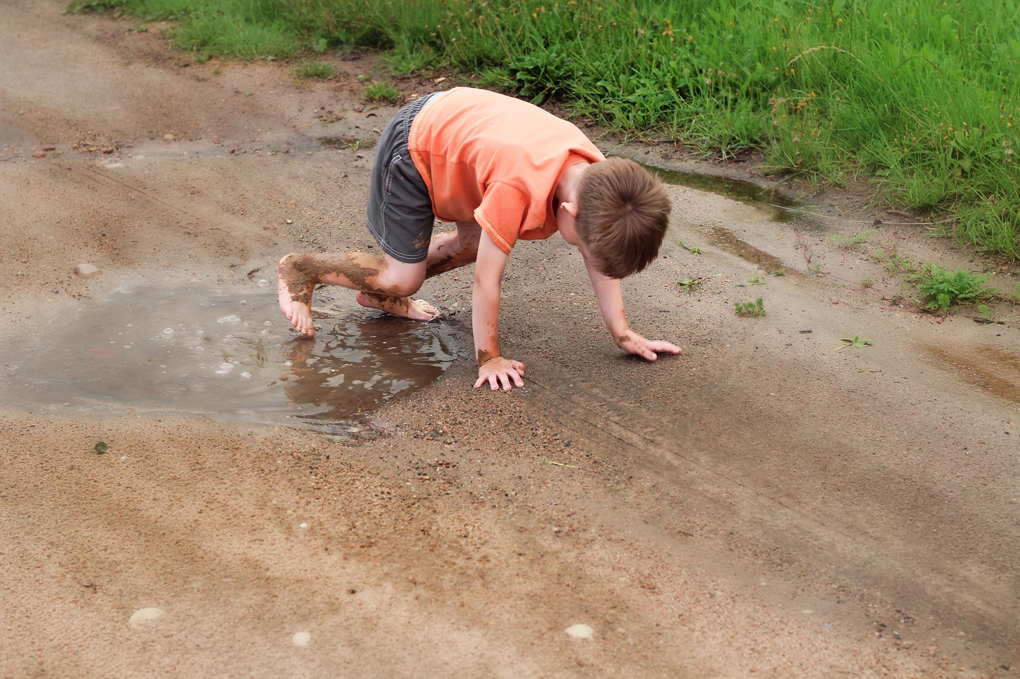 мальчик играет в луже на деревенской дороге