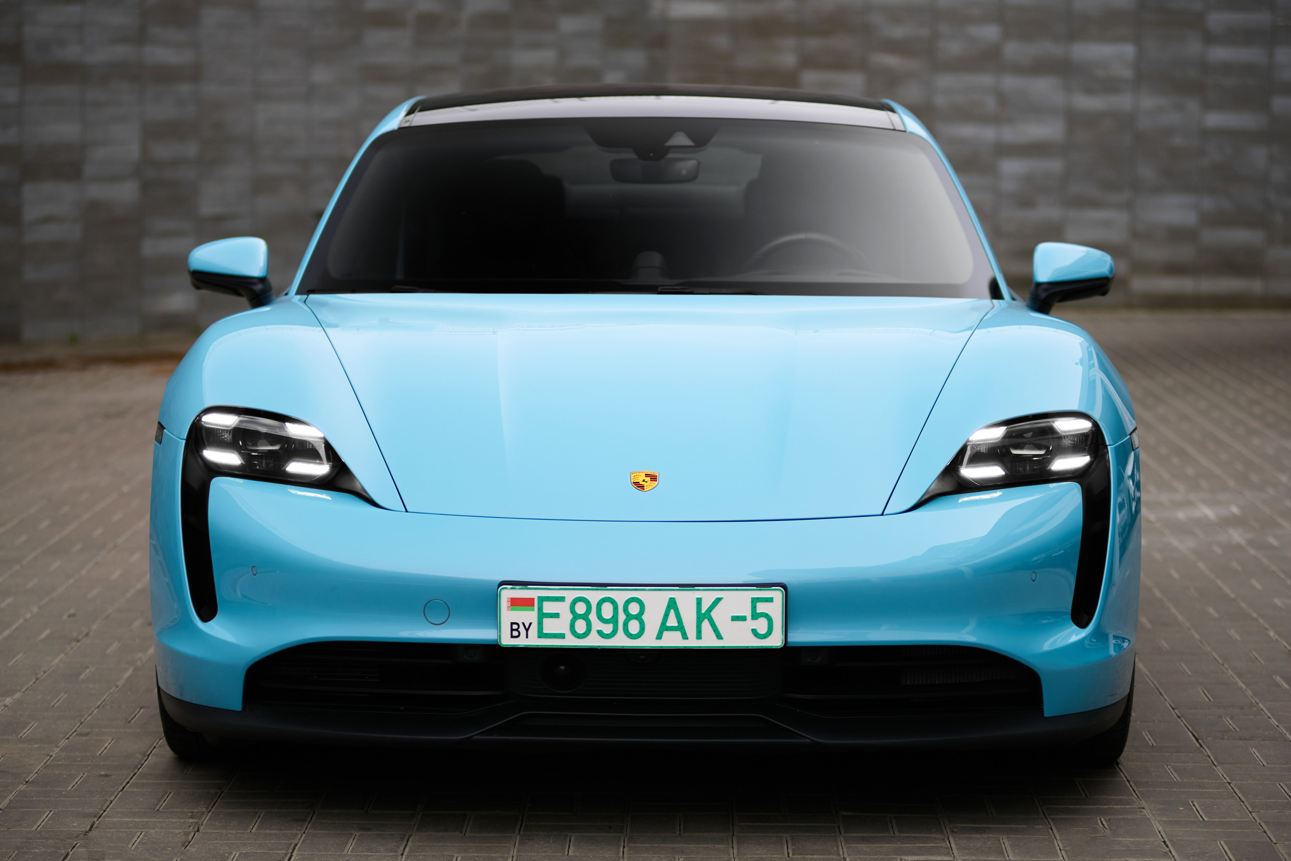 Голубой Porsche Taycan 4S спереди на фоне серой стены