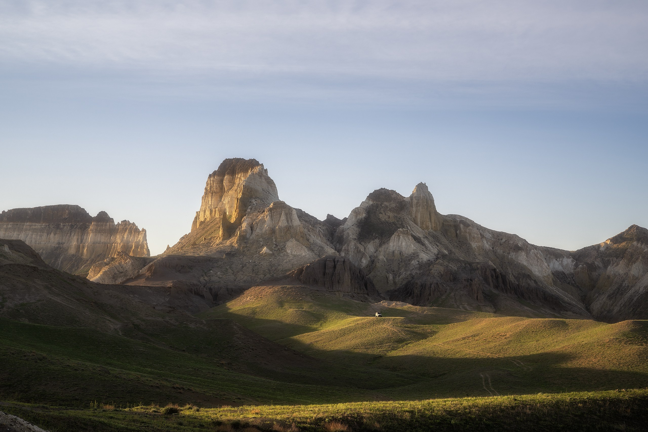 Утро в горах Мангистау, горы освещены солнцем и на дальнем плане в горах стоит машина