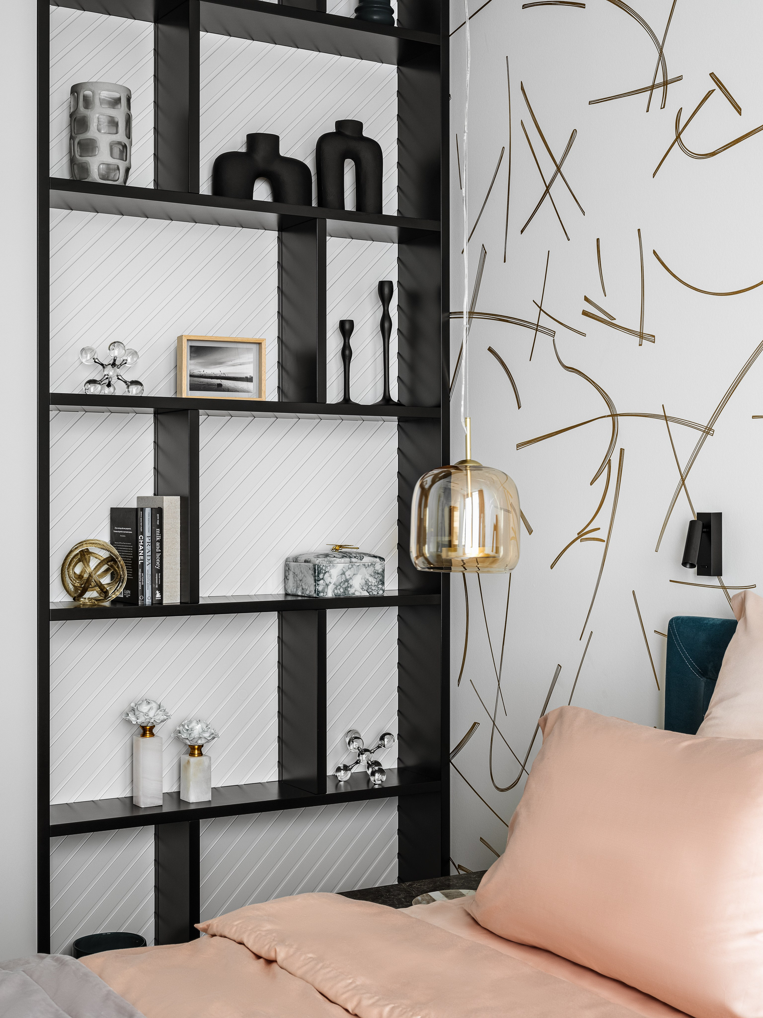 Интерьер спальни с декоративным стеллажом черного цвета, наполненным стильными аксессуарами, графичной отделкой стены и текстилем нежного оттенка. Проект создан Ренатом Байчуковым и Алисей Кириенко, стилизован Екатериной Ракитиной, снят Сергеем Денисенко.