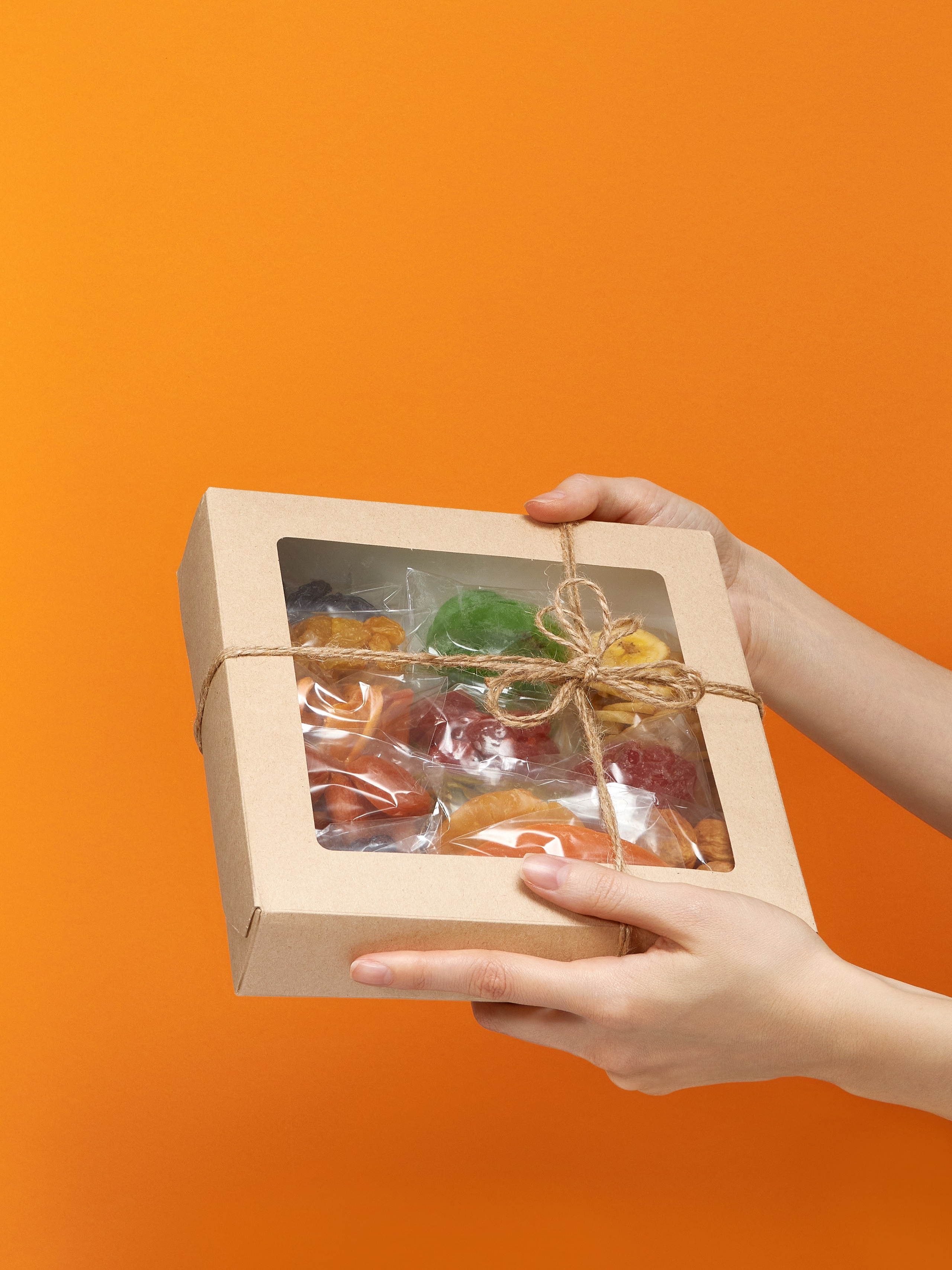 Предметная рекламная фотосъёмка подарочного набора орехов и сухофруктов на оранжевом фоне в руках модели