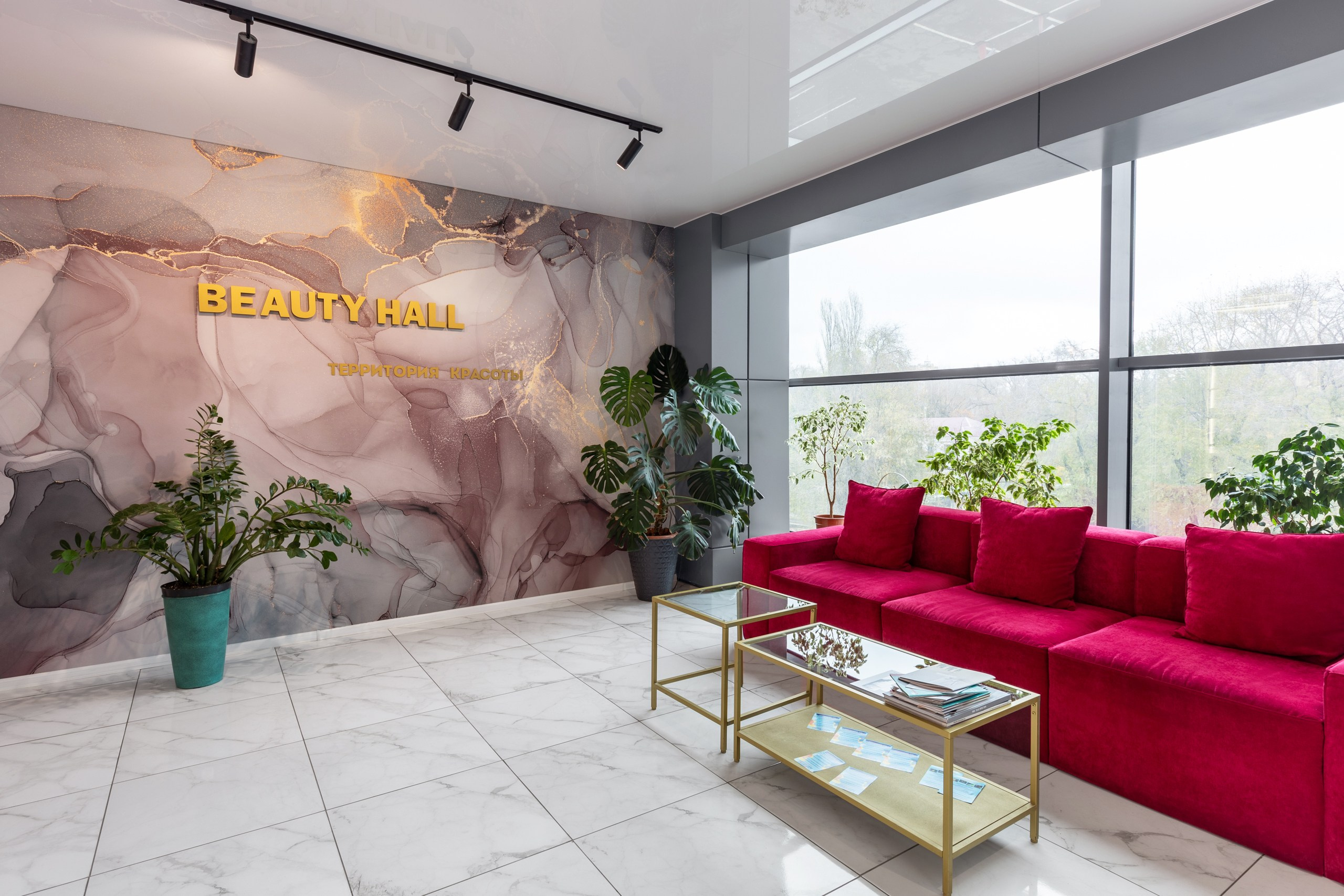 Салон красоты в Воронеже. Стена под мрамор, яркий розовый красный диван и стеклянный столик в холле салона.