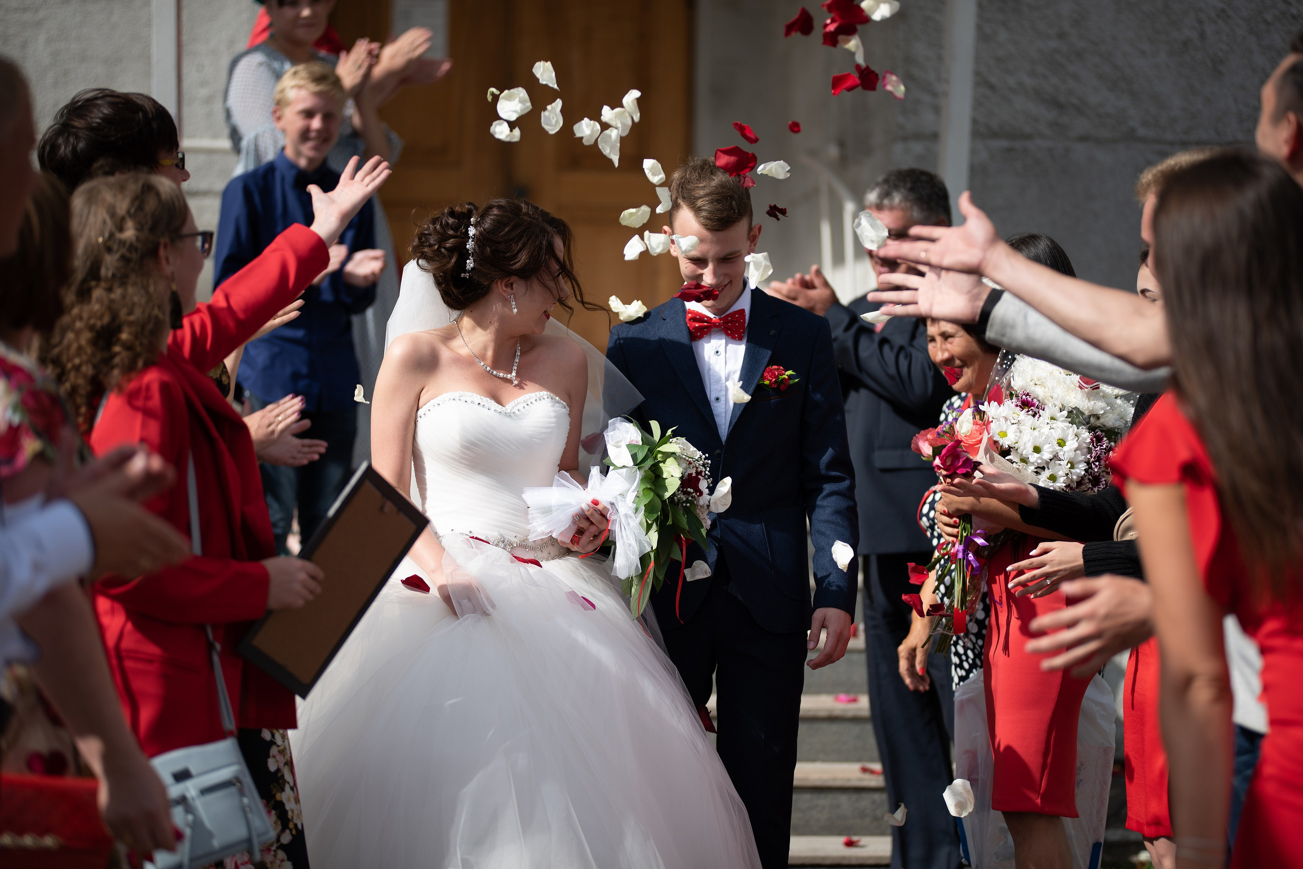 Свадебный фотограф успел поймать момент, когда в кадр летят лепестки роз и молодожены выходят из ЗАГСа.