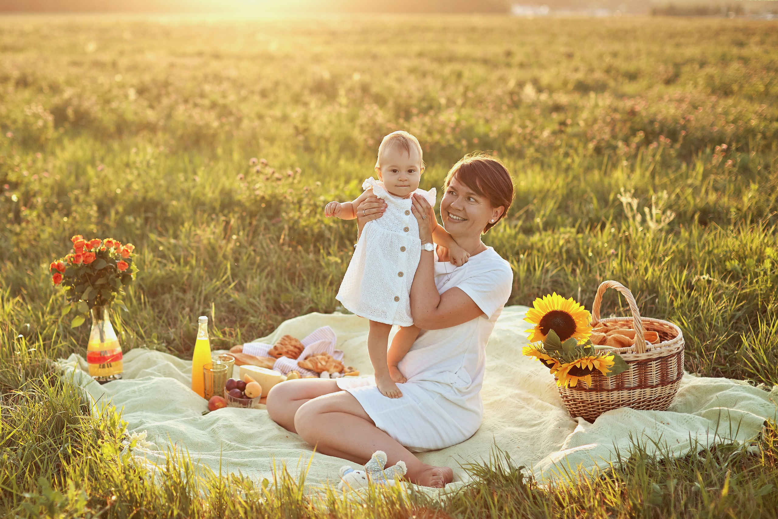 мама с дочкой в белых платьях сидят в поле на пикнике и закатный свет красиво их освещает